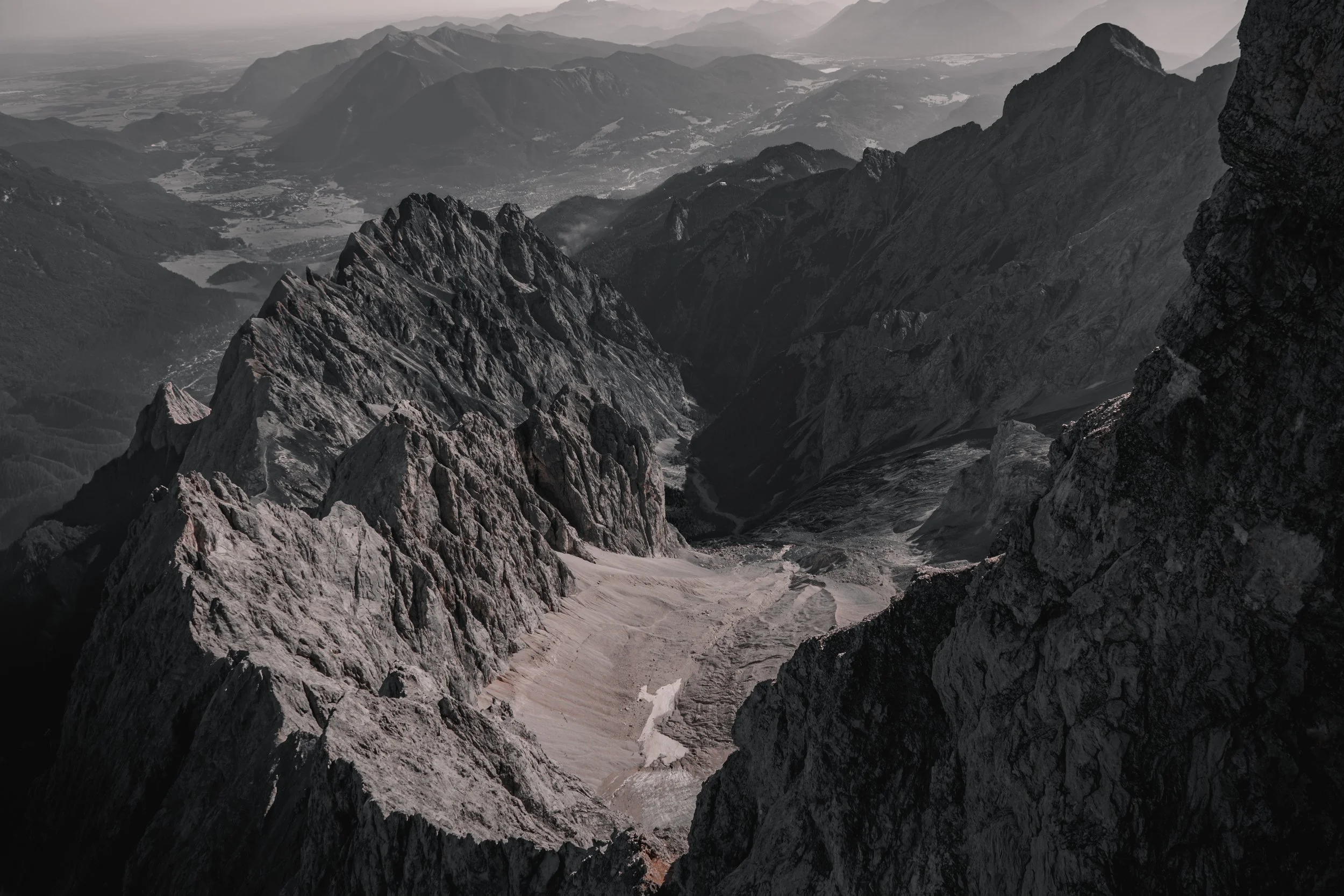 Felsgrat und Gebirgstal
Blick über schroffe Felsgrate und ein tiefes alpines Gebirgstal bis zur gestaffelten Berglandschaft am Horizont – Bergfotografie von ReBlick.