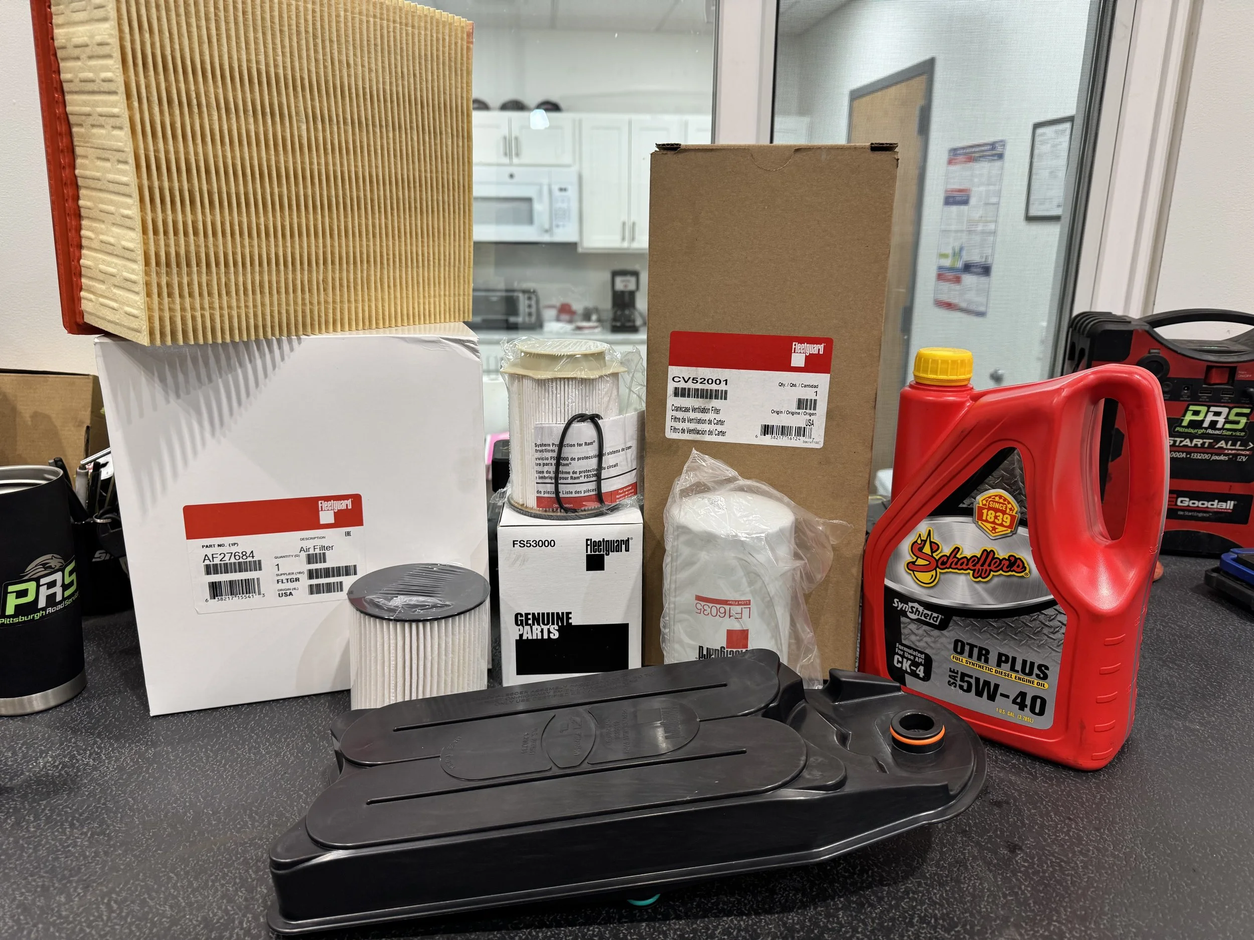 Car parts and supplies on a workbench, including an air filter, fuel filter, oil, and various boxes and containers.