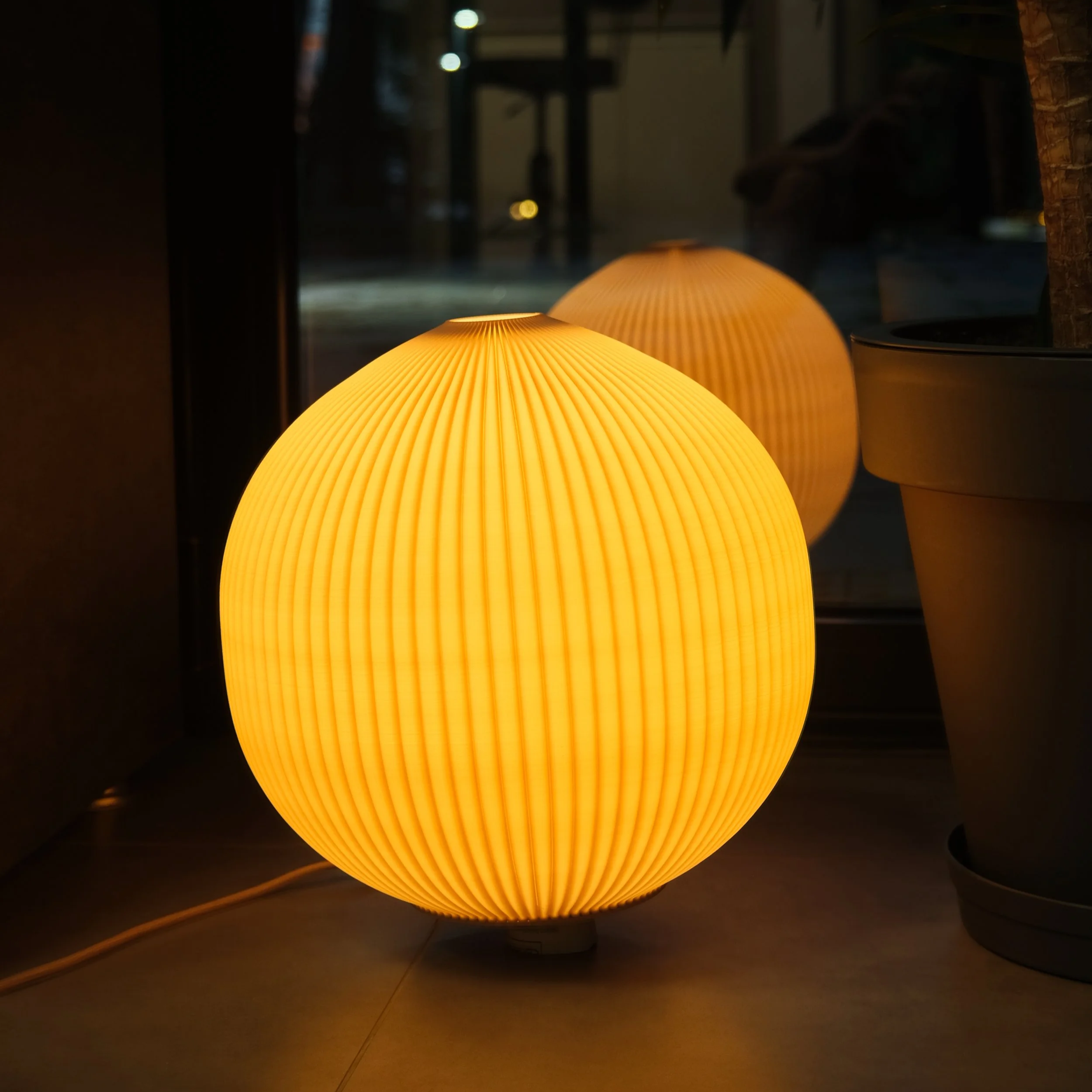 A glowing round yellow paper lantern with vertical ridges, placed on the floor near a window.