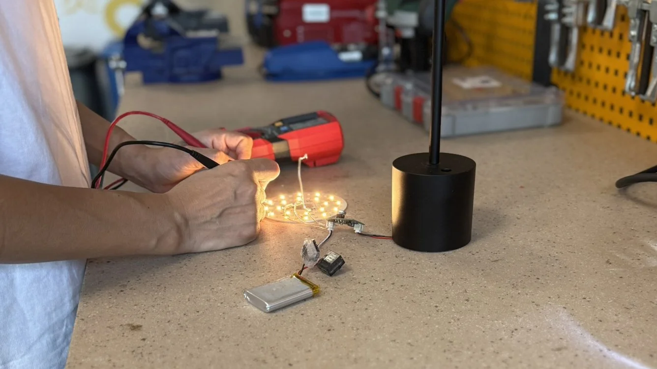 Person working on a small electronic circuit with LEDs on a workshop table, using multimeter and other tools.