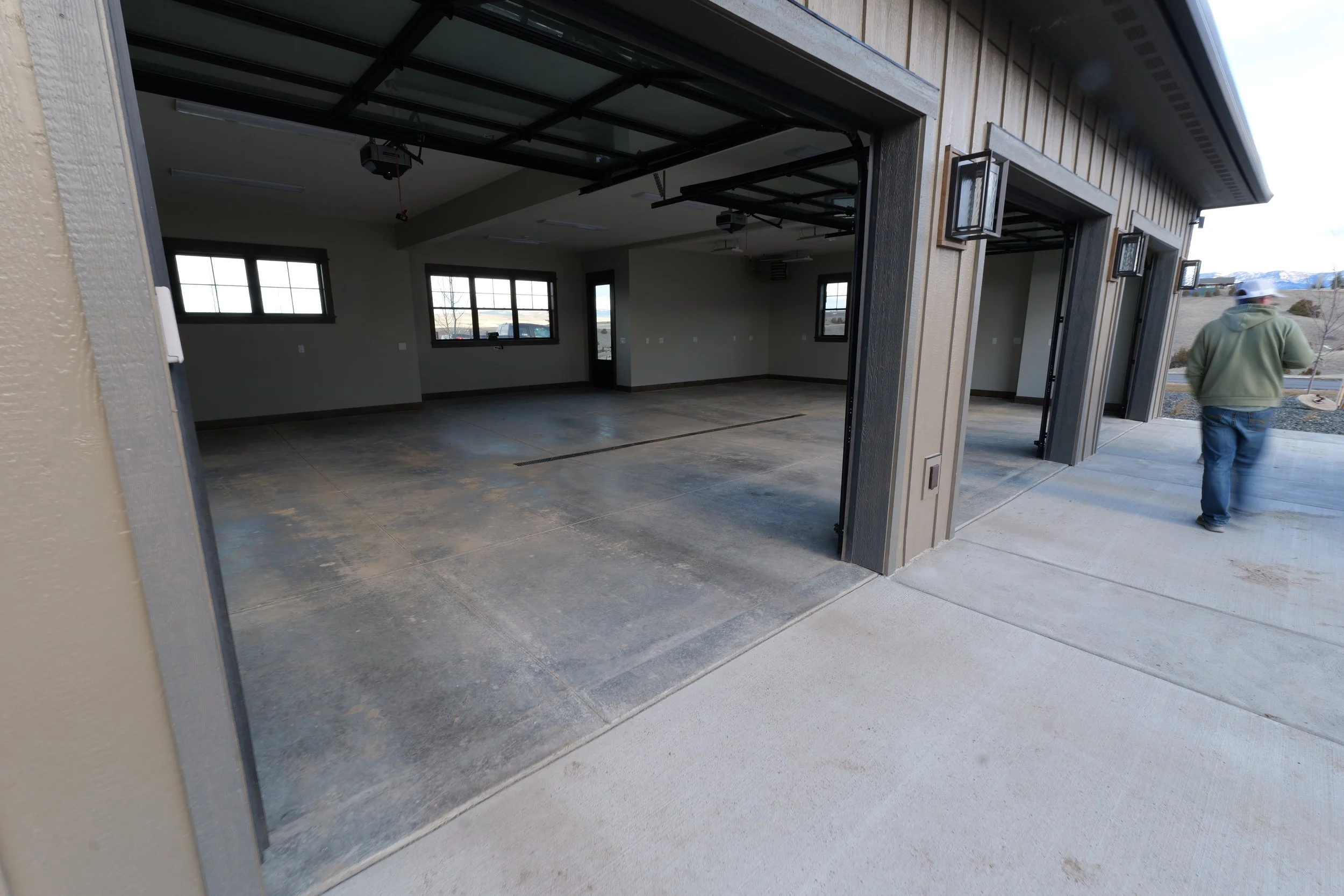 Empty garage with open doors, concrete floor, multiple windows, and a man walking away from the garage outside.