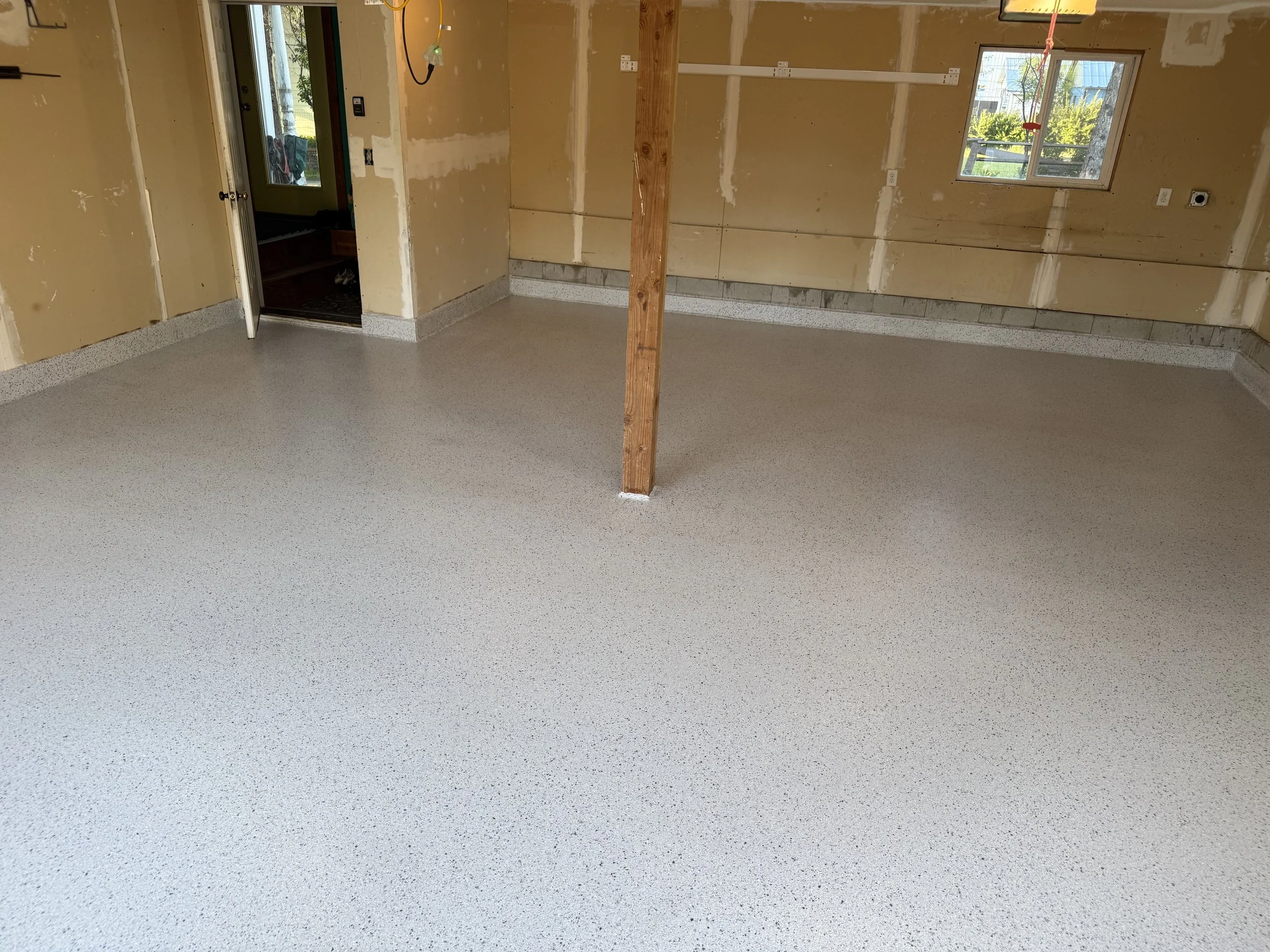 Empty room with newly installed epoxy flooring, partially finished drywall walls, and two windows for natural light.