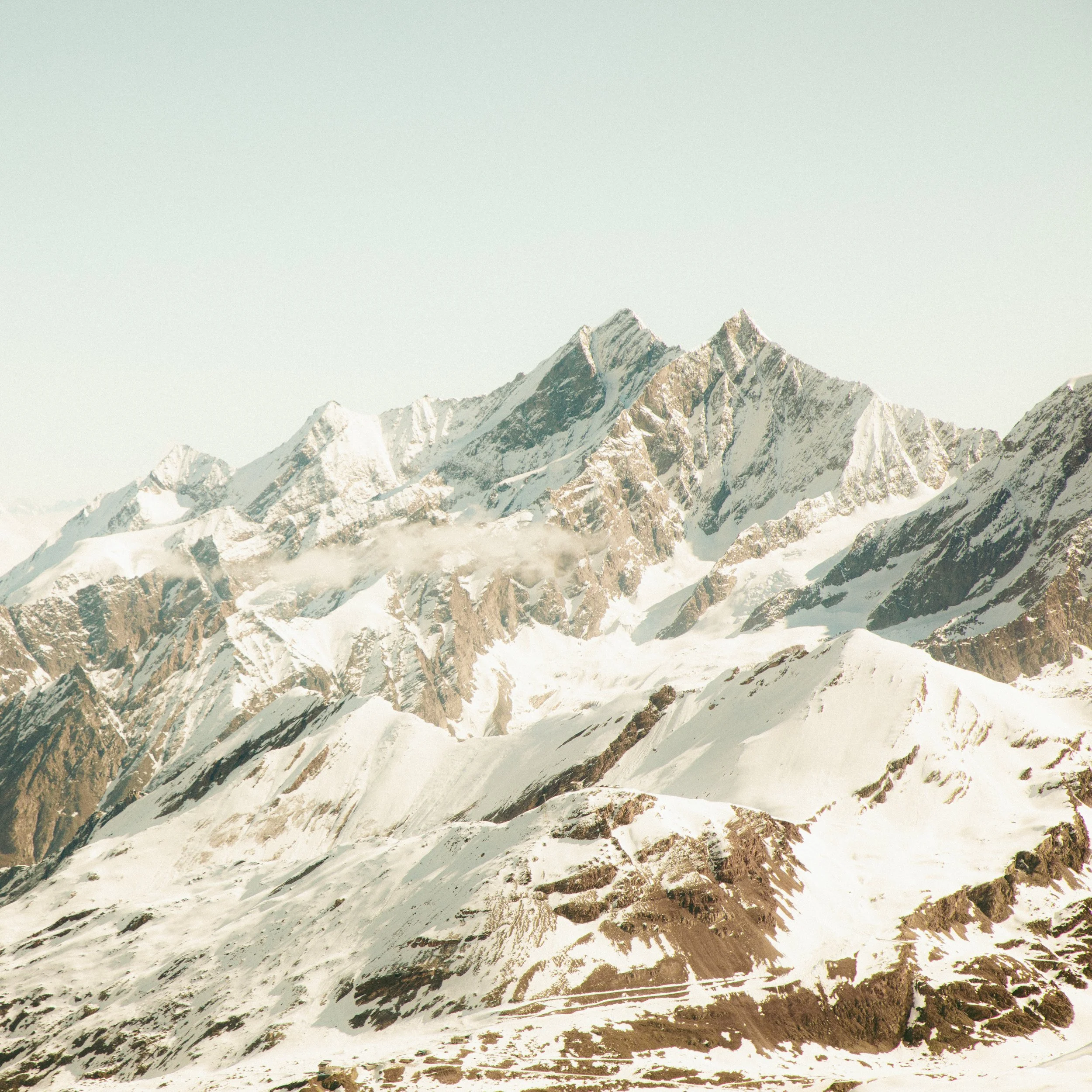 Snow-covered mountain peaks under a pale, clear sky