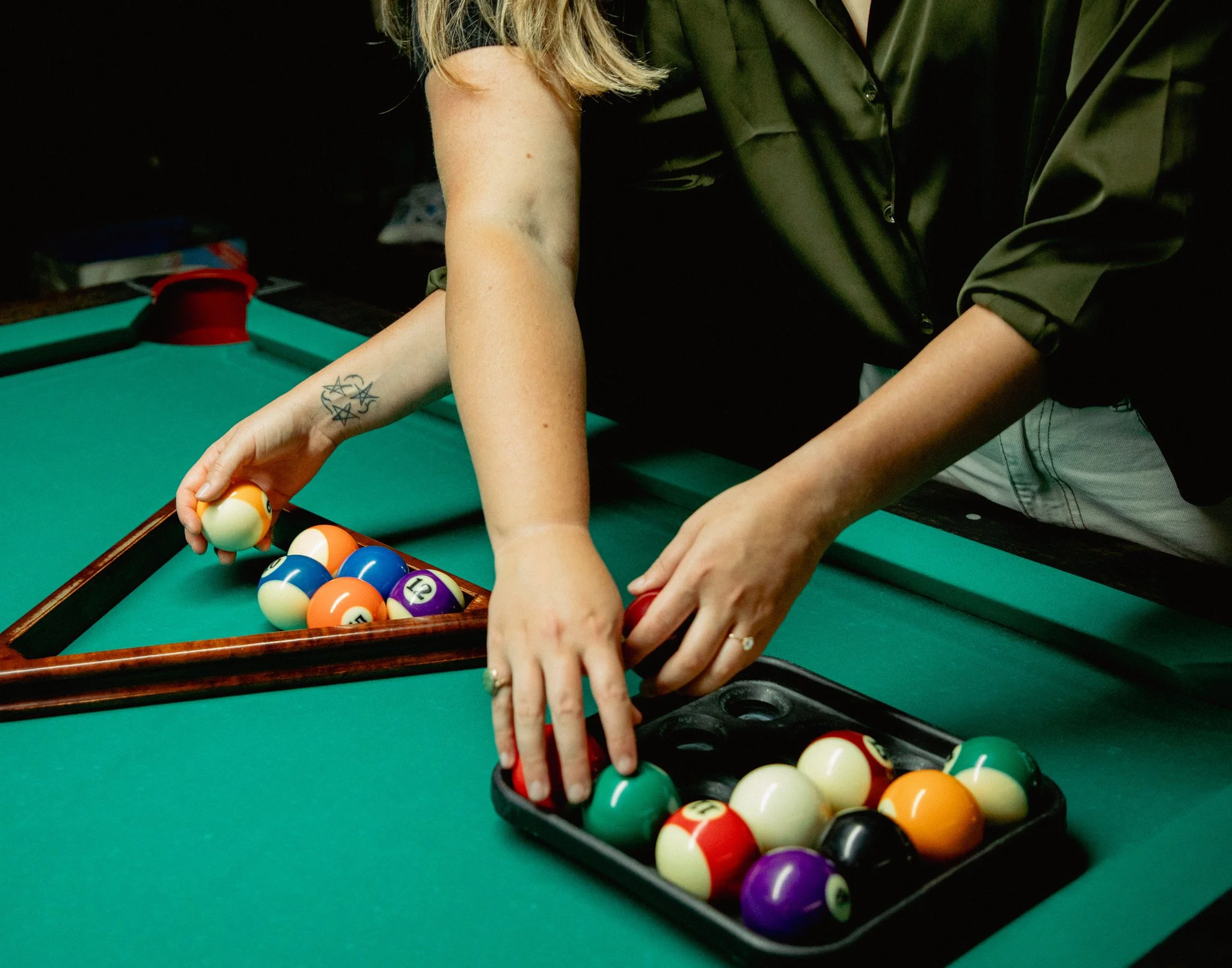 People playing pool at a pool table with billiard balls arranged for a game.