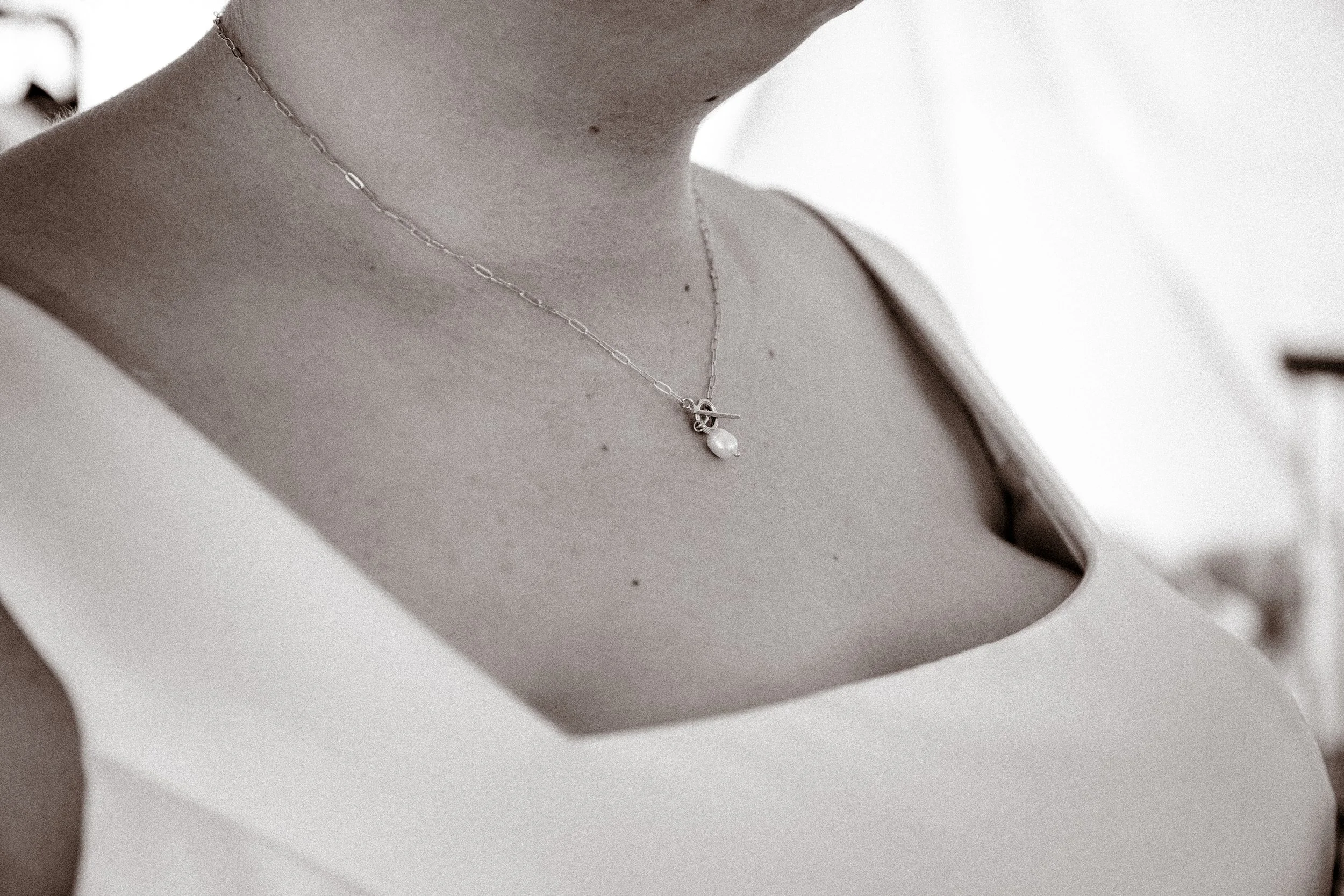 Close-up of a woman's neck and upper chest wearing a delicate necklace with a pearl pendant.