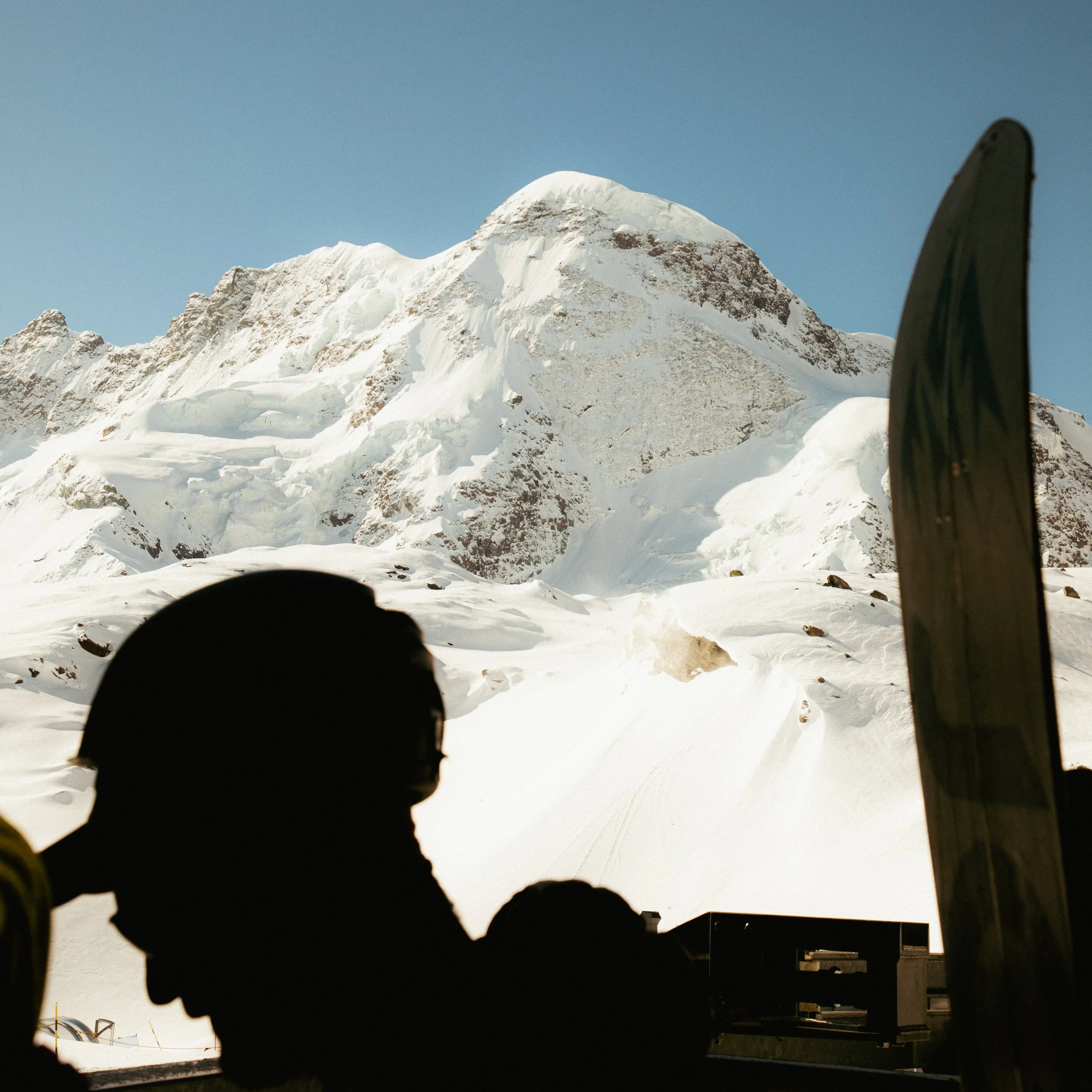 Snow-covered mountain peaks against a clear blue sky, with some buildings and equipment in the foreground.