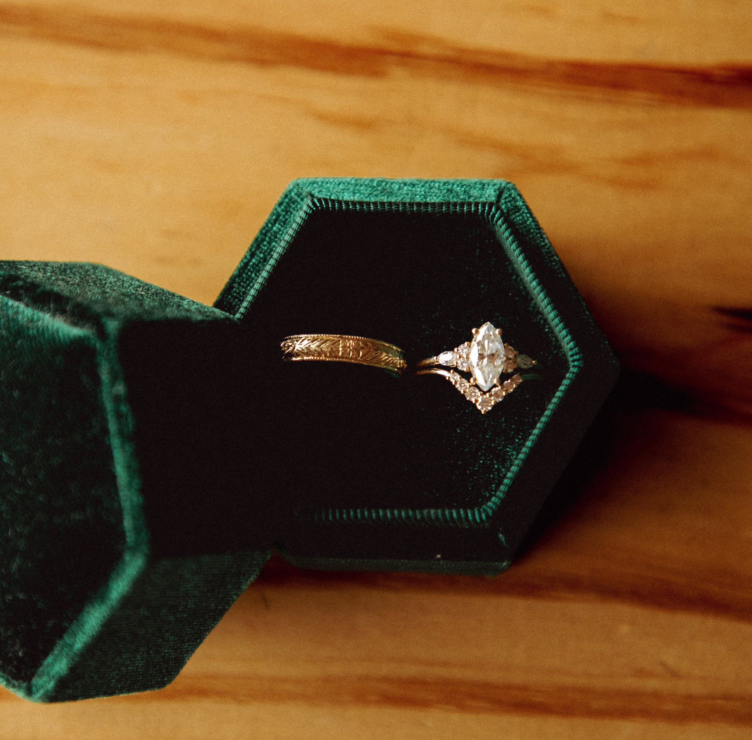 Close-up of a jewelry box on a wooden surface, containing a gold ring and a large diamond ring.