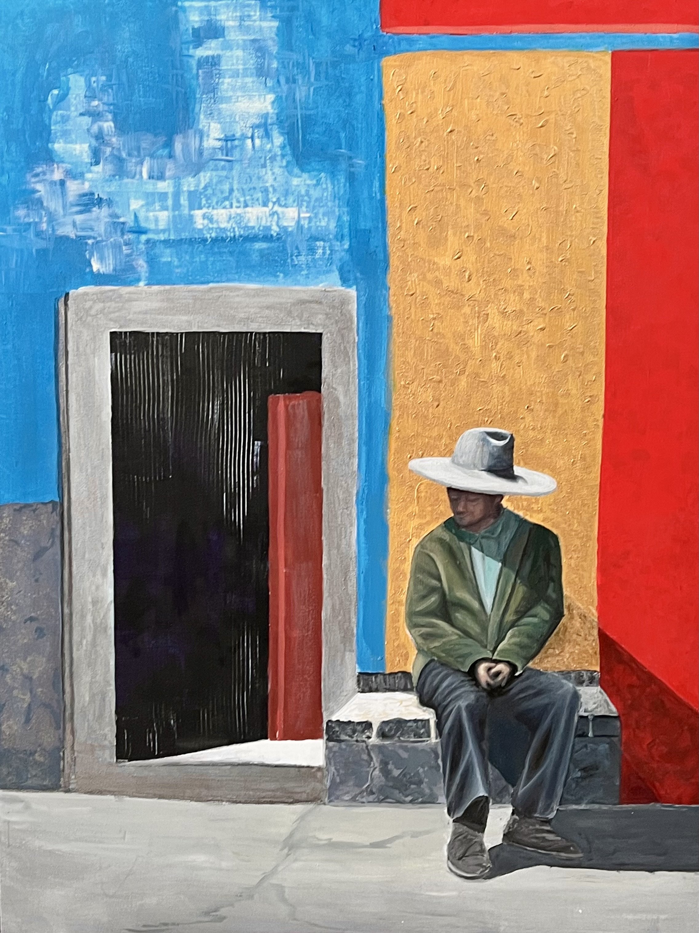 A man sitting on a bench against a colorful wall, wearing a wide-brimmed hat, green jacket, and gray pants, with a red-painted door and vibrant yellow, red, and blue sections of wall behind him.