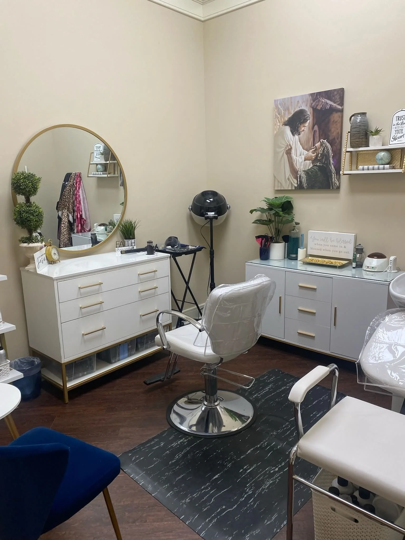 Interior of a makeup or beauty salon room with a white styling chair, a white dresser mirror, and various decorative items on shelves and countertops.