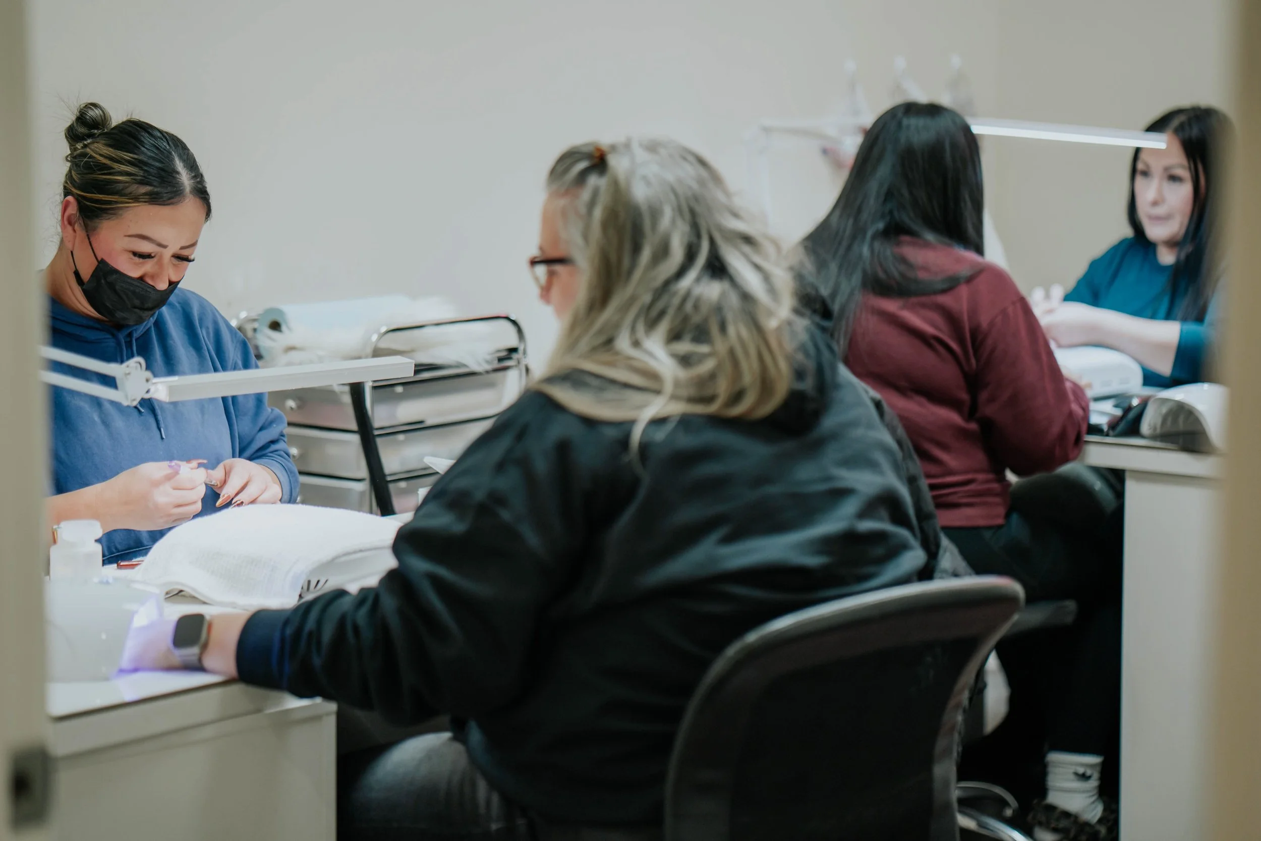 Nurses working at a nail salon, performing nail treatments on clients, with supplies and equipment on the tables.