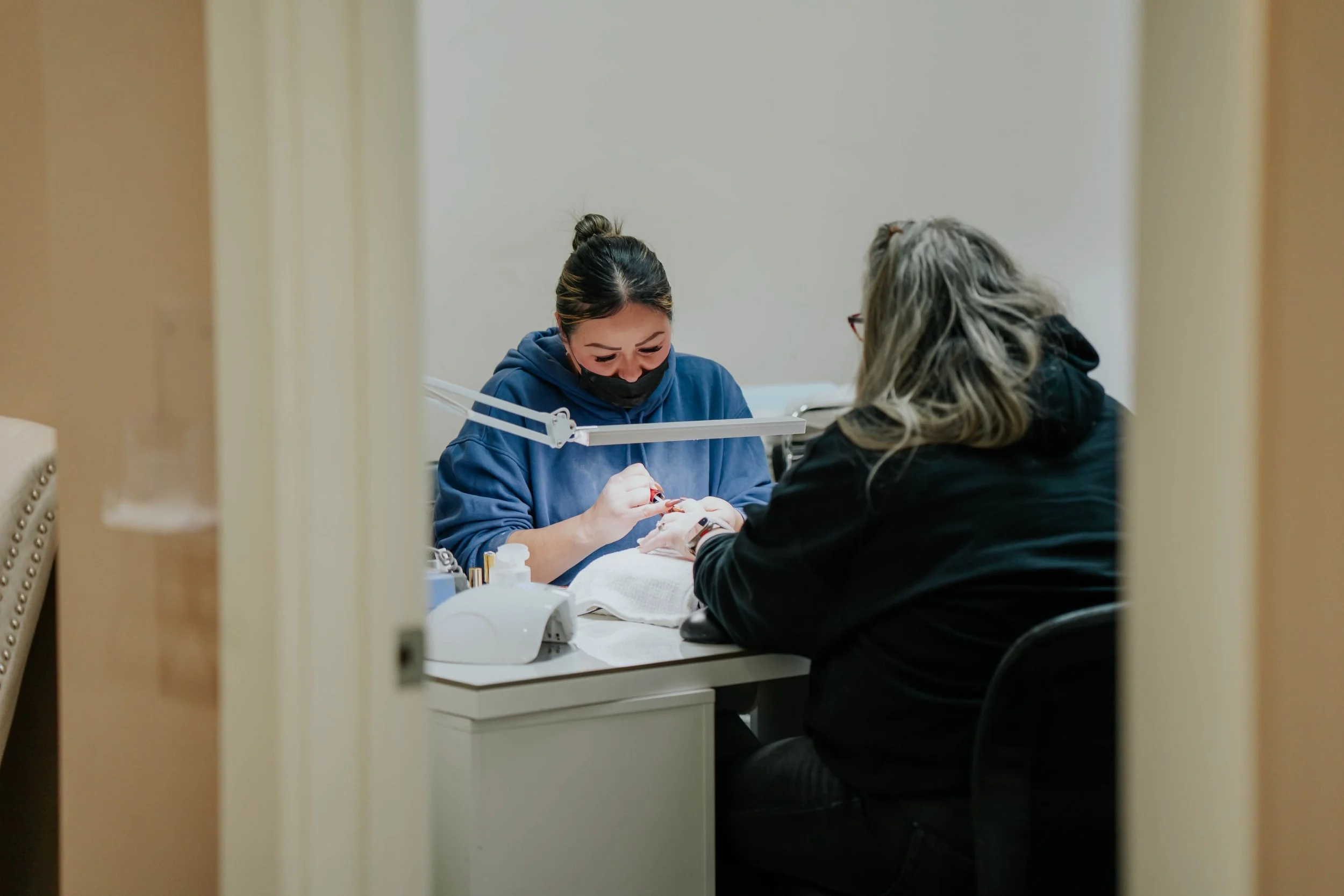 A woman receiving a manicure from a nail technician in a salon