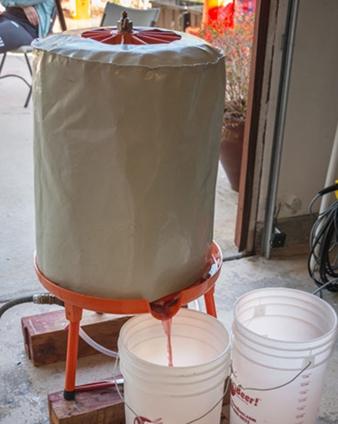 A homebrewing setup with a fermentation bucket, a wrapped fermentation vessel, and tubing for extracting beer.