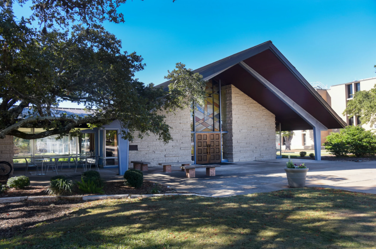 Gold chalice holding a round white host with a rosary hanging on its side, set against a blurred background with a gold cross.