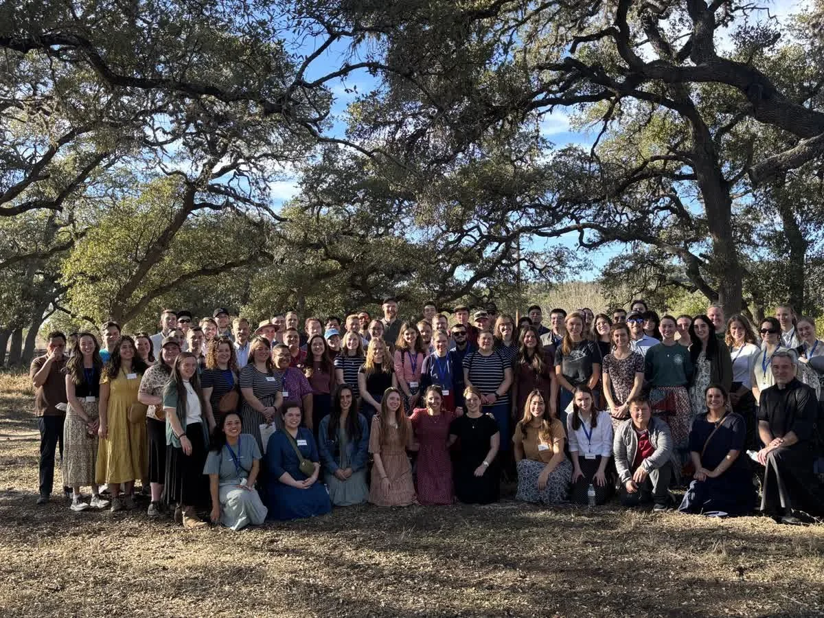 A large group of people gathered outdoors under trees on a sunny day, posing for a photo.