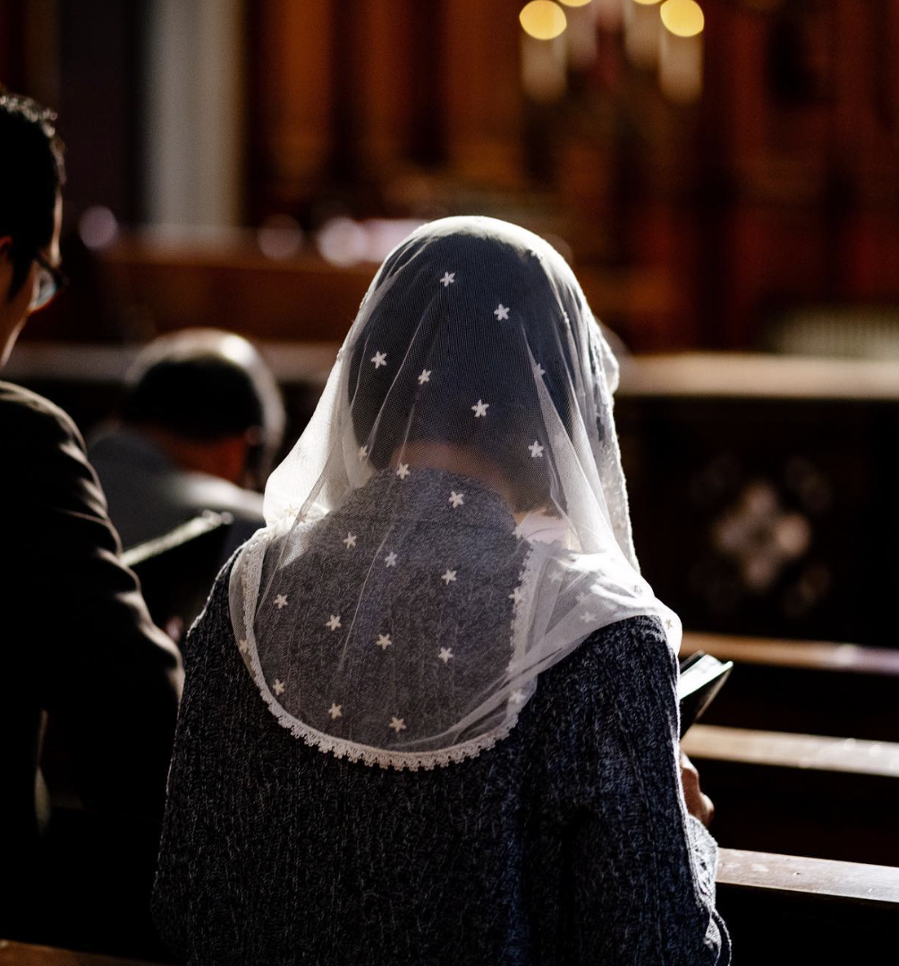 Woman with a star-patterned veil reading a cellphone in church.