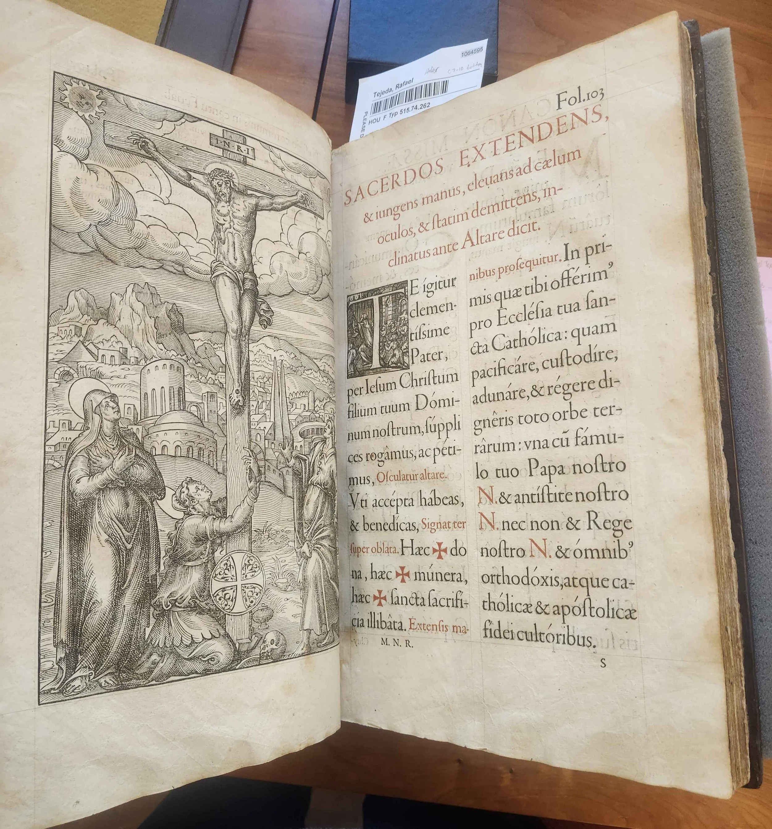 Page from an old religious book showing a detailed black-and-white illustration of Jesus Christ on the cross with two figures on either side, against a city background, and Latin text on the adjoining page.