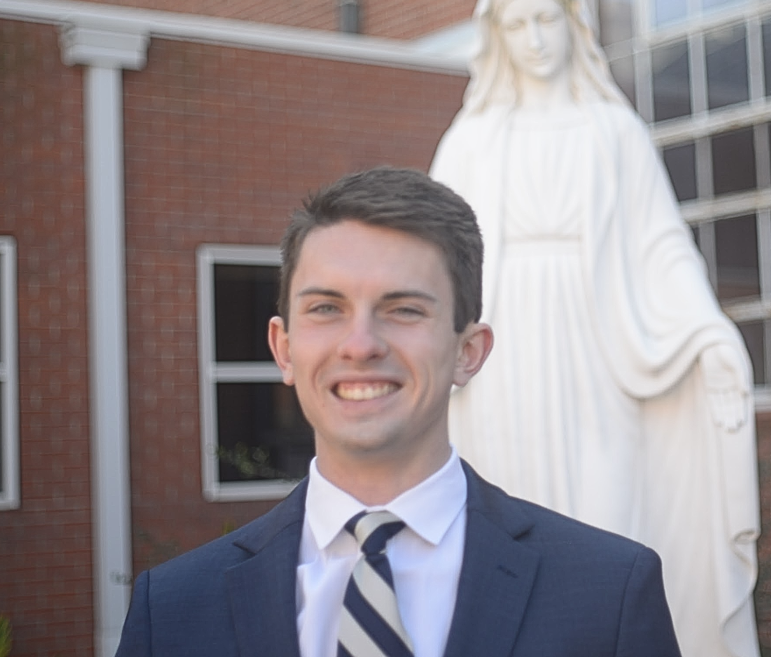 A young woman with shoulder-length black hair smiling in a greenhouse with green plants.