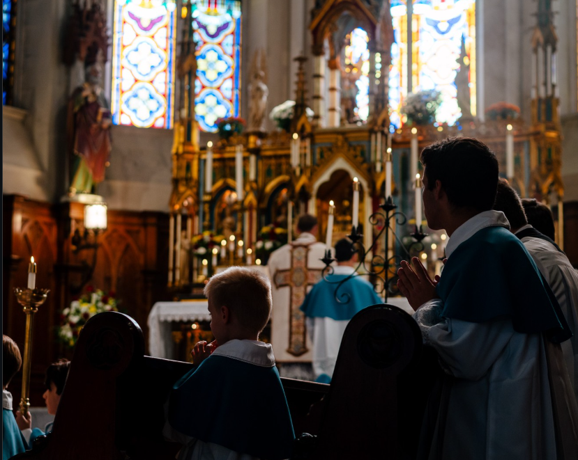 A modern wooden house with large glass windows is situated in a grassy field at the base of a mountain range.