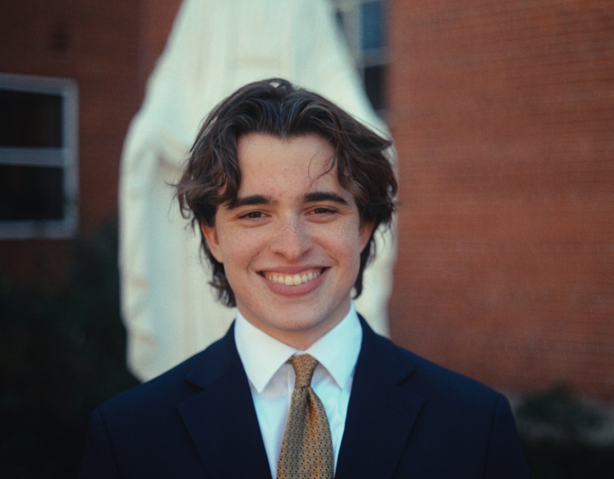A smiling woman with glasses and curly hair, wearing hoop earrings and layered necklaces, in an indoor setting.