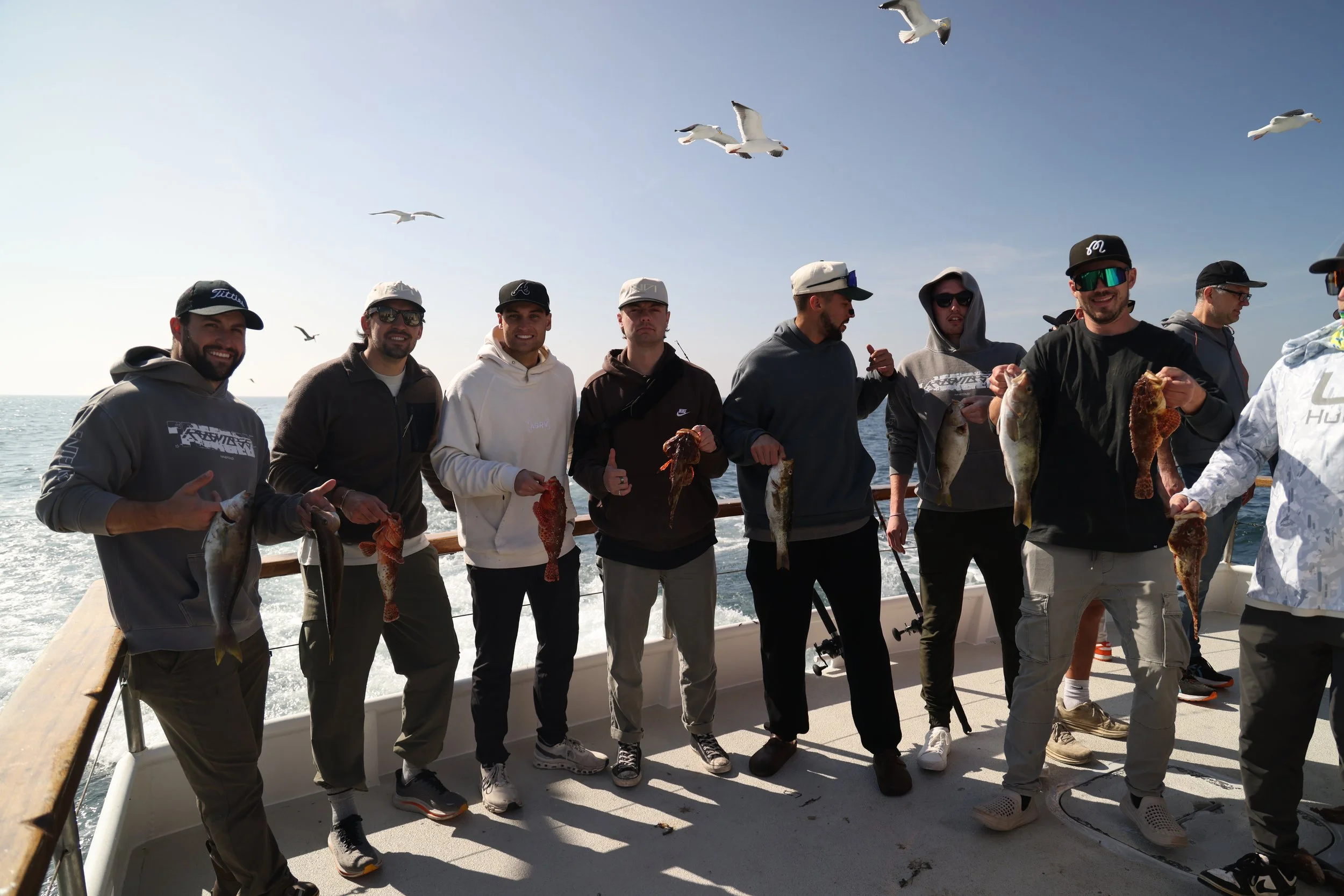 Ninefold Leadership Trip. Group of nine men standing on a boat holding fish they caught, with seagulls flying overhead on a clear day at sea.