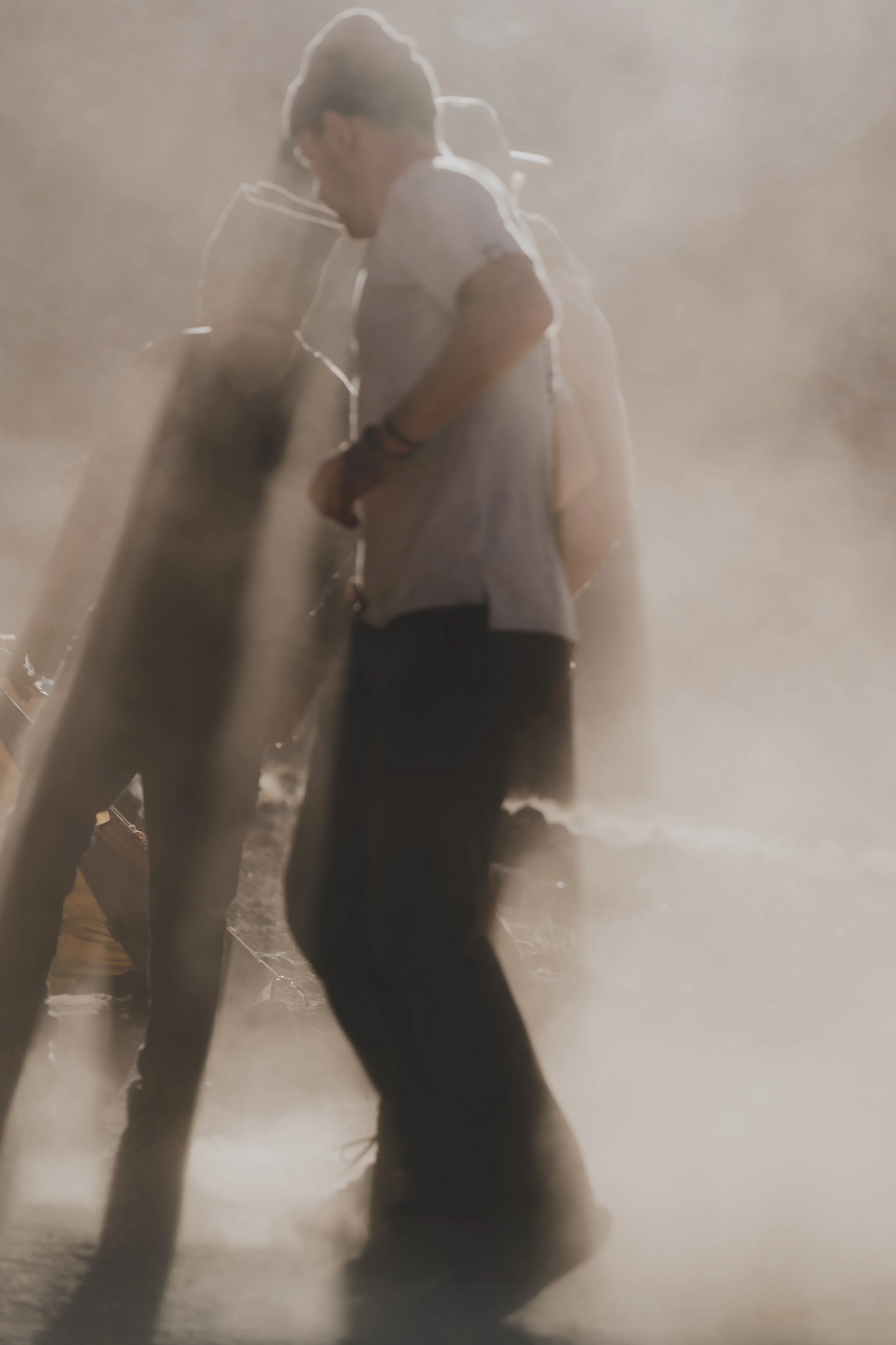 Ninefold Bucklist Trip. People standing in a foggy or dusty environment, with one person wearing sunglasses, a white shirt, and a backpack, looking downward.
