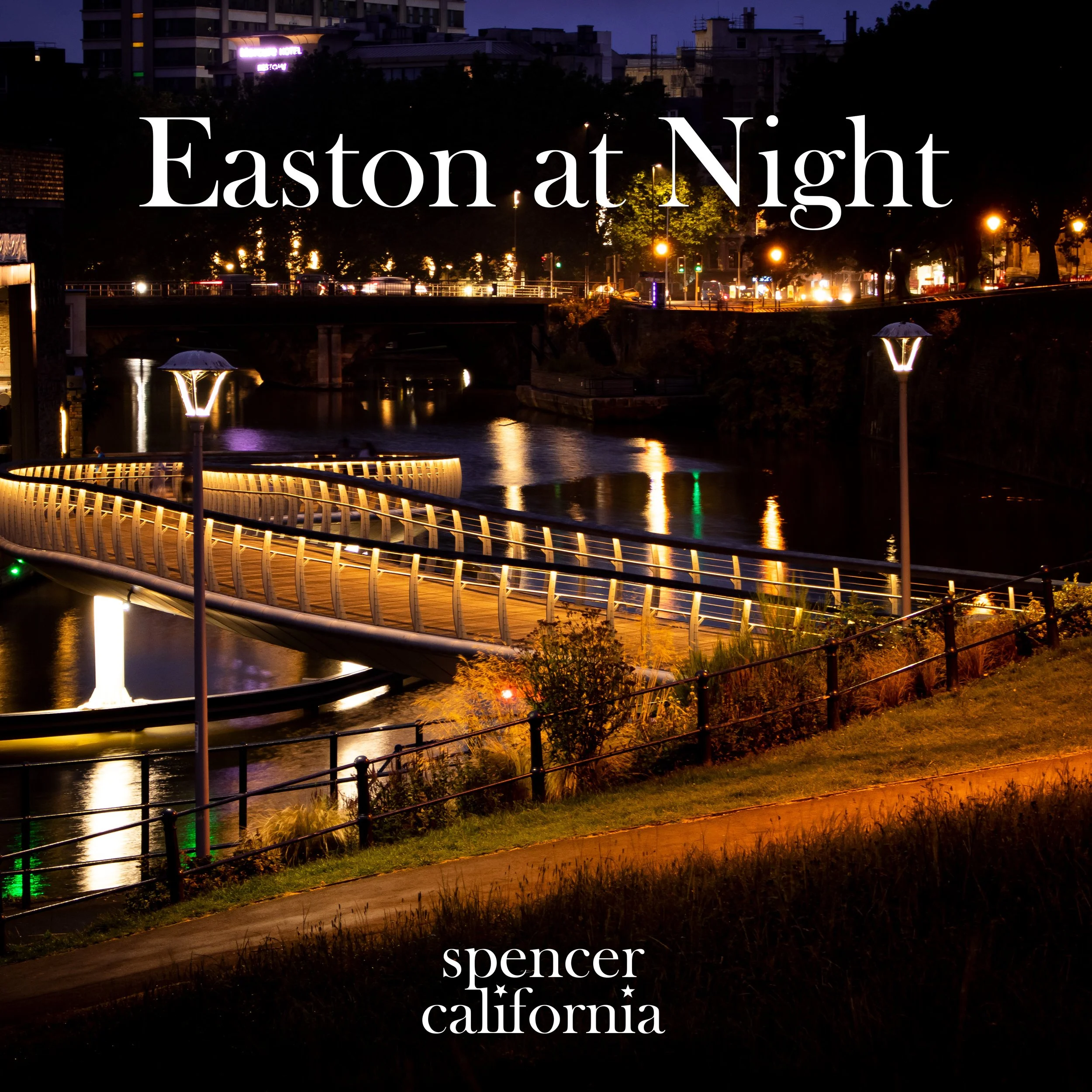 Night view of a bridge over a river in Easton (A neighbourhood in Bristol), illuminated by streetlights, with city lights and buildings in the background.