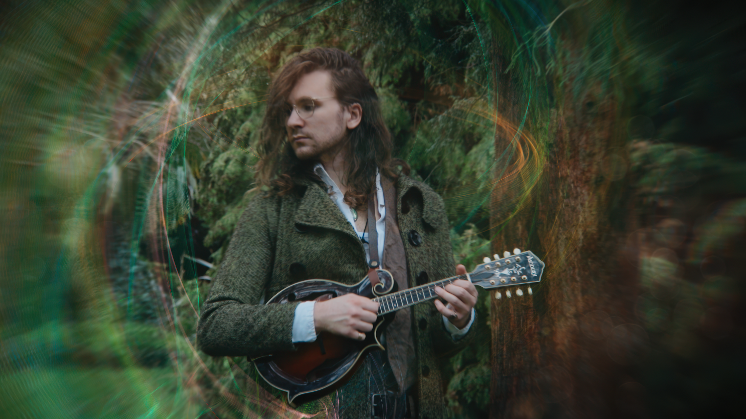 A young man with long hair and glasses playing a mandolin outdoors in a forest, with colorful abstract light effects surrounding him.