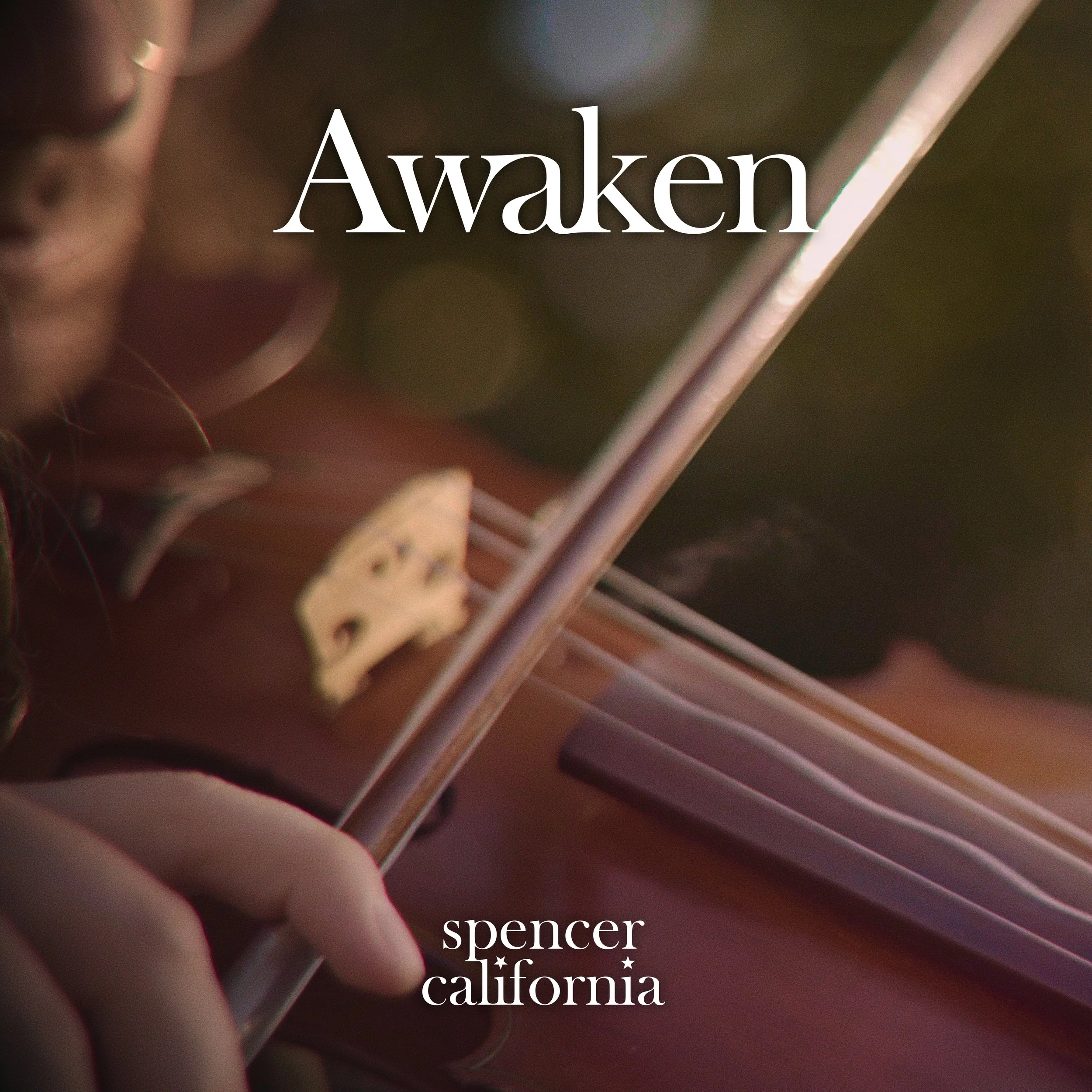 A close-up of a hand playing a violin, with the word 'Awaken' overlaid and the text 'spencer california' at the bottom.