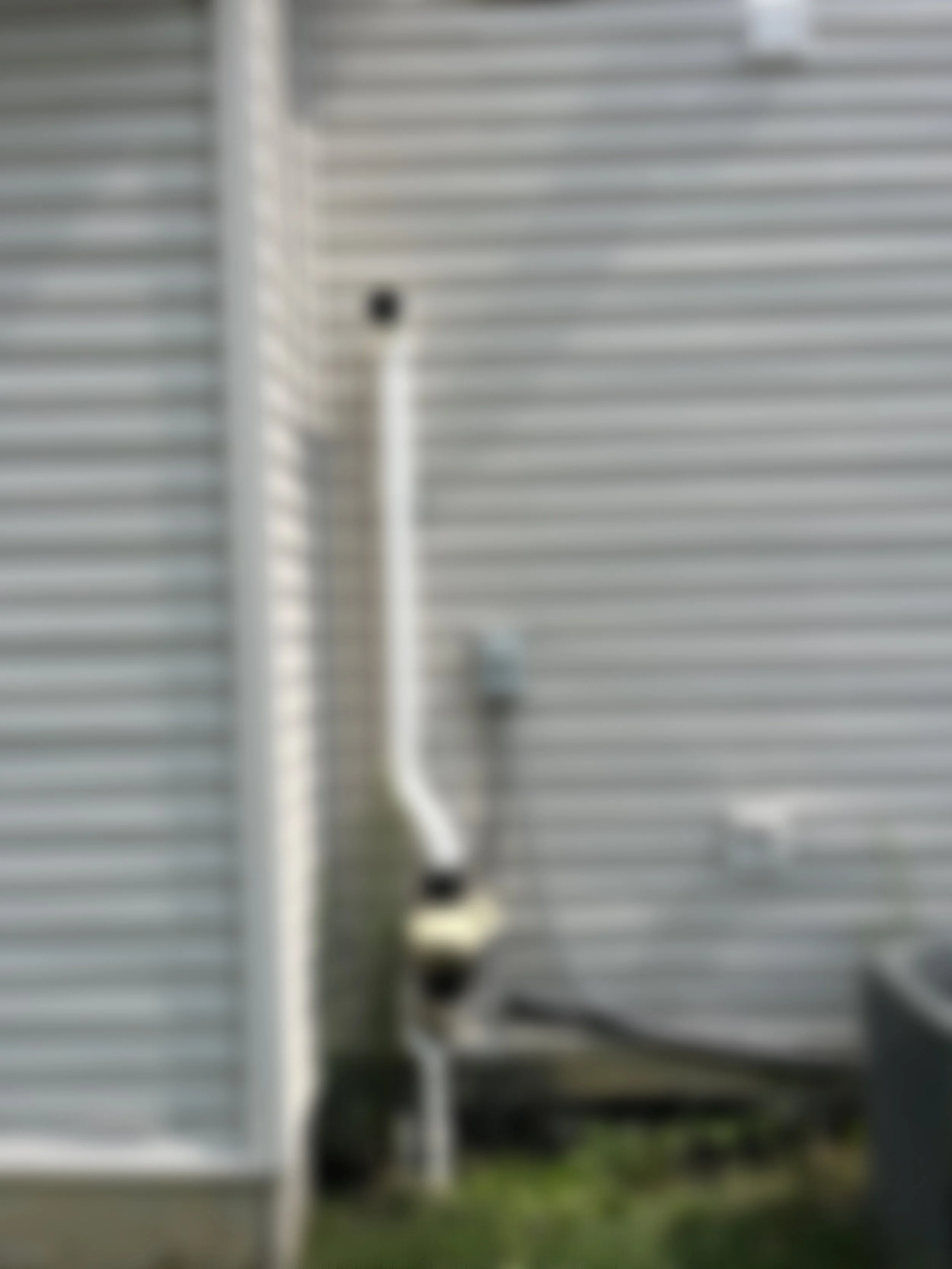 Blurred image of a utility pipe and a vent pipe attached to a corrugated metal building wall.