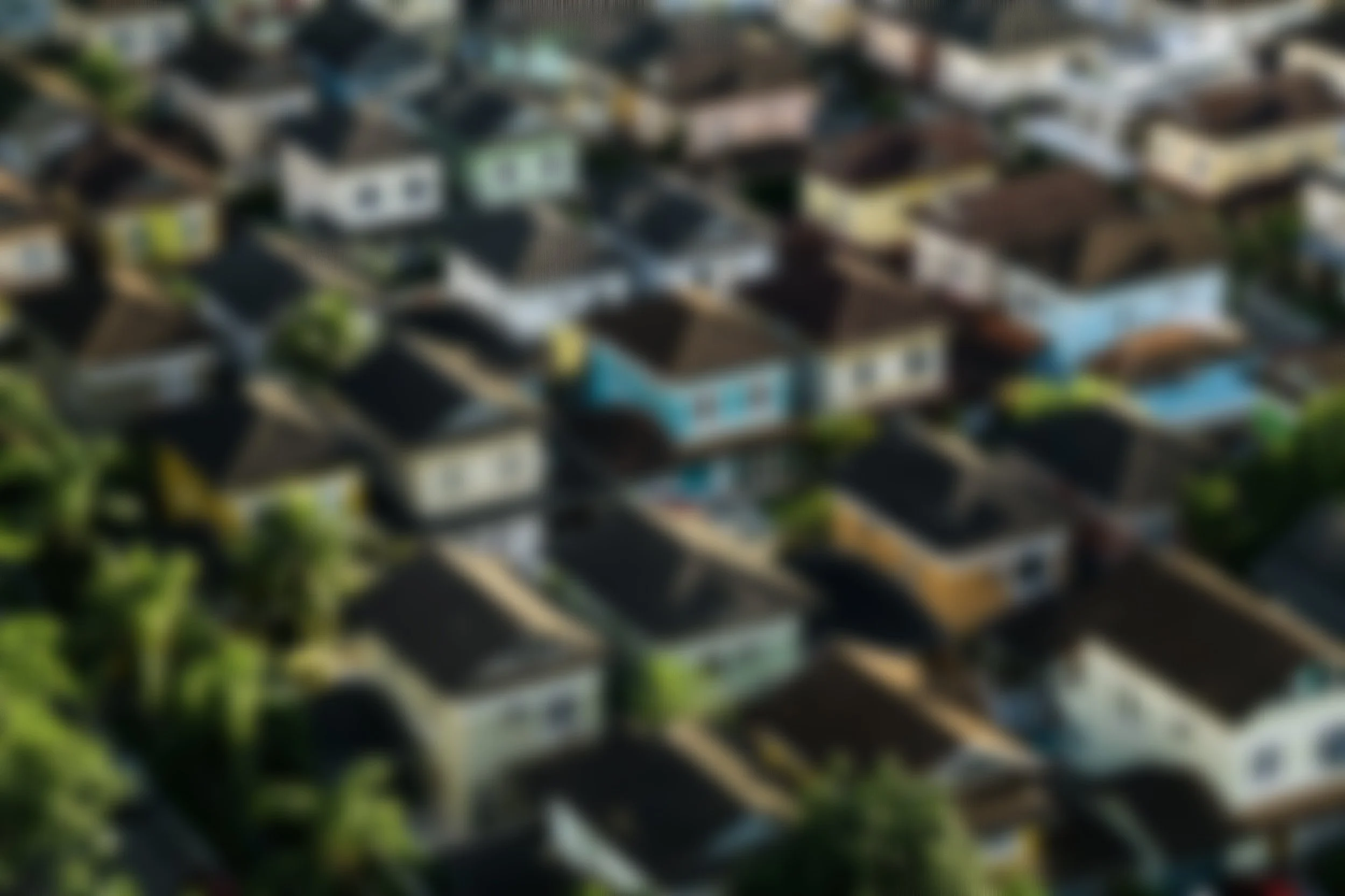 Blurred aerial view of a neighborhood with multiple houses and rooftops.