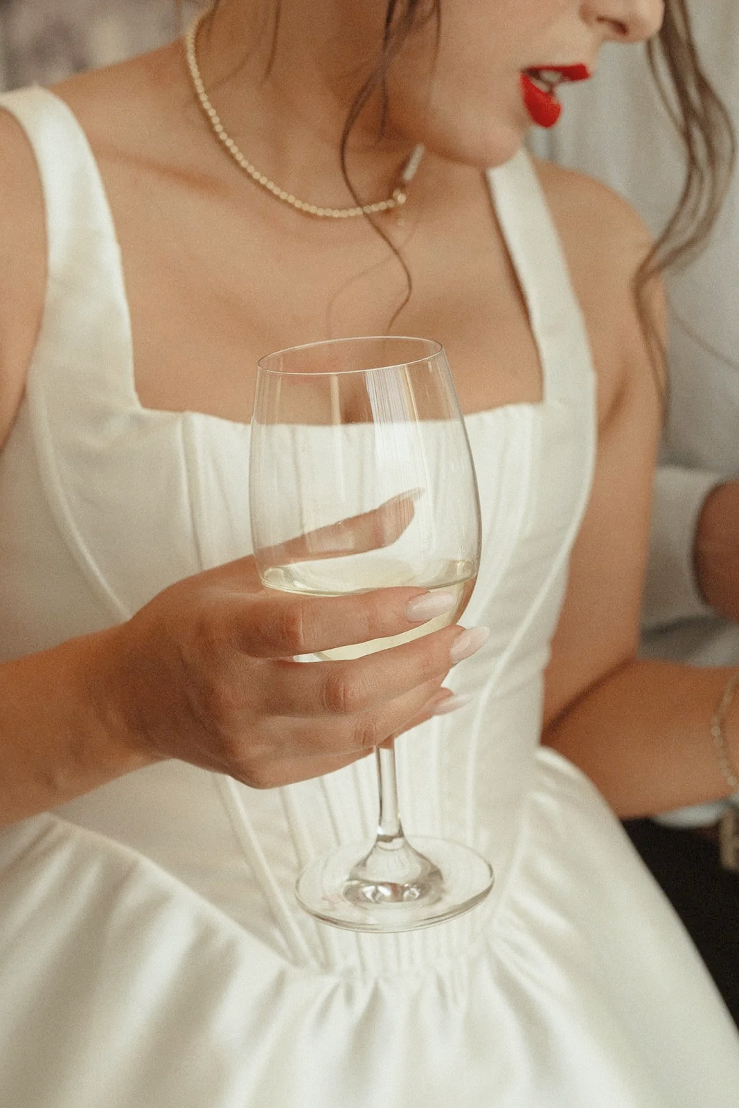 A woman in a white dress holding a glass of white wine at a social gathering.