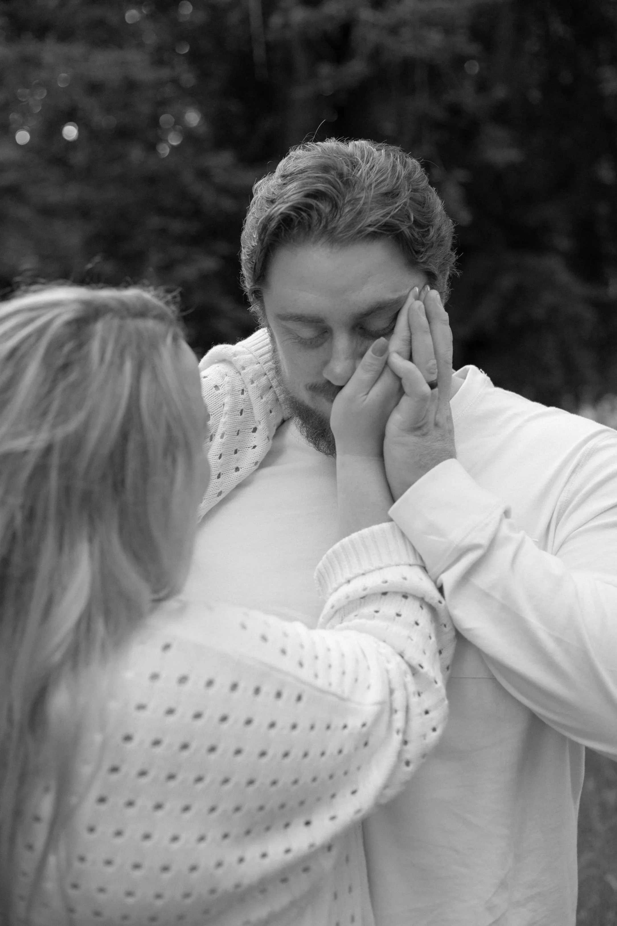 Black and white engagement photo. Groom embraces brides hand on face.