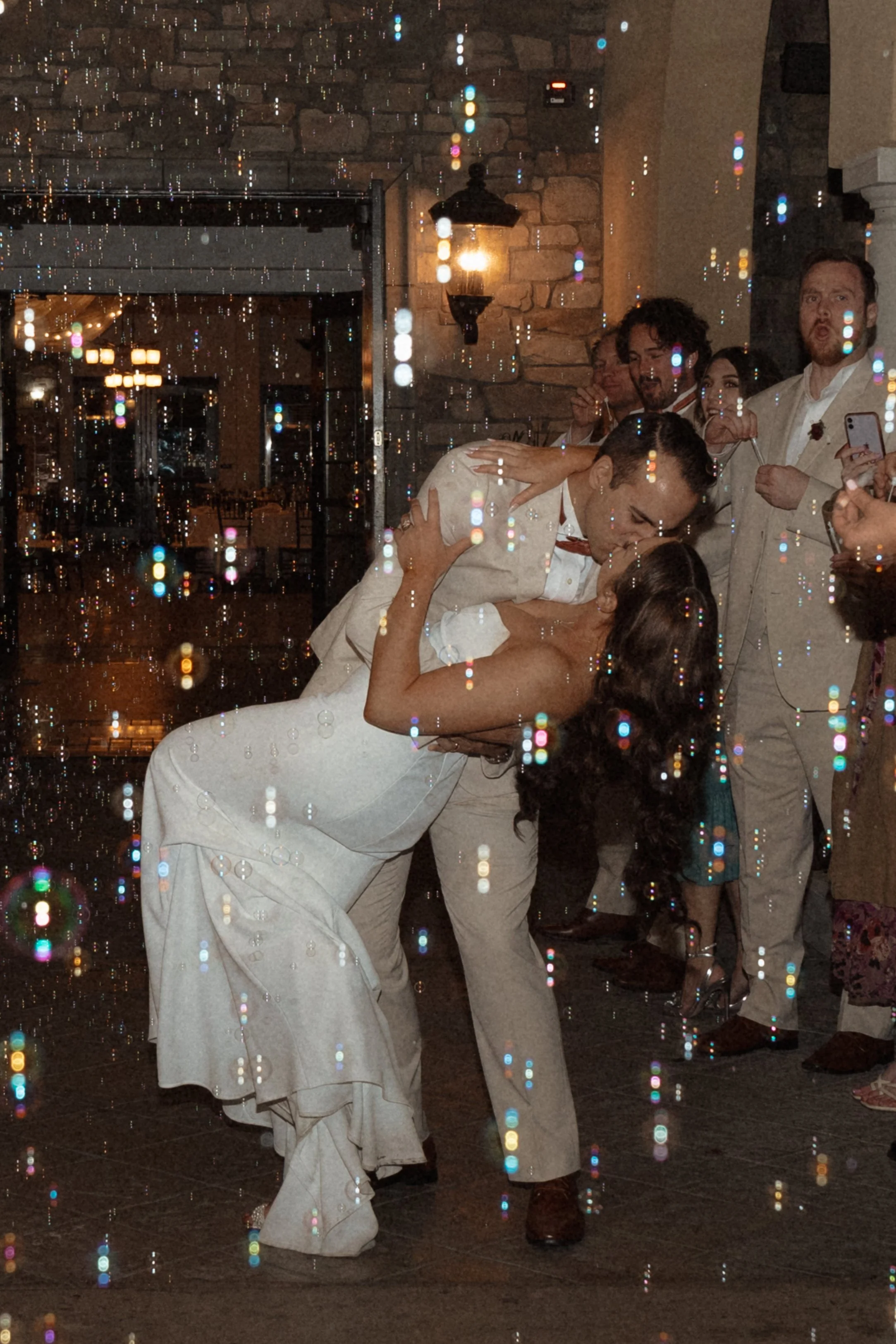A couple dancing closely at their wedding reception, surrounded by guests, with sparkling effects overlayed.