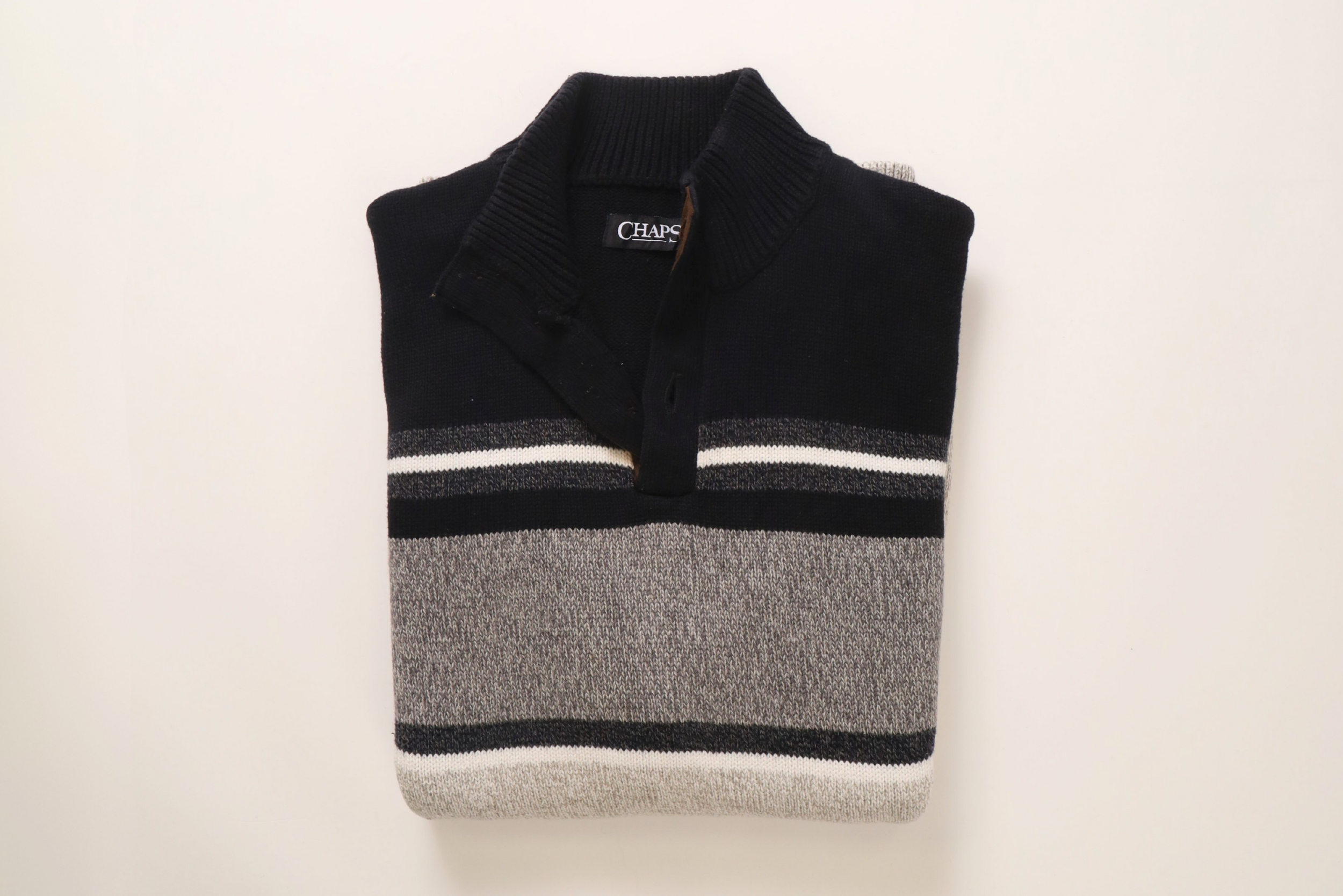 A folded vintage men's striped sweater with black, white, and gray horizontal bands, featuring a collared neckline with a button placket, on a white background.