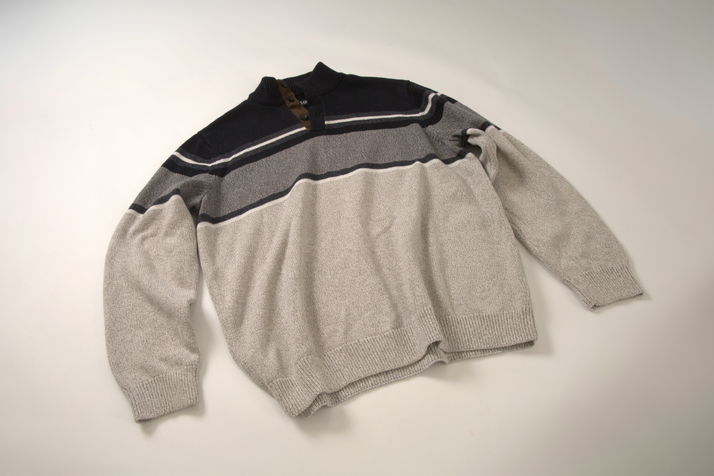 Neutral striped vintage jumper with a black collar and buttons laid flat on a white surface.