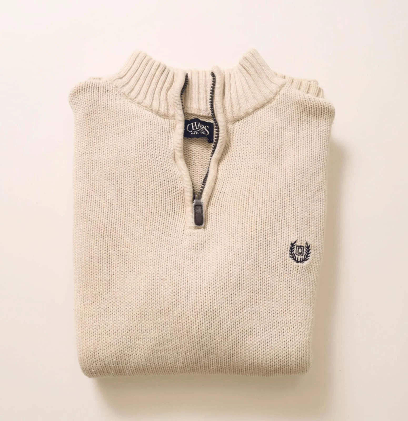Folded beige knitted sweater with a quarter-zip collar and a embroidered logo on the chest