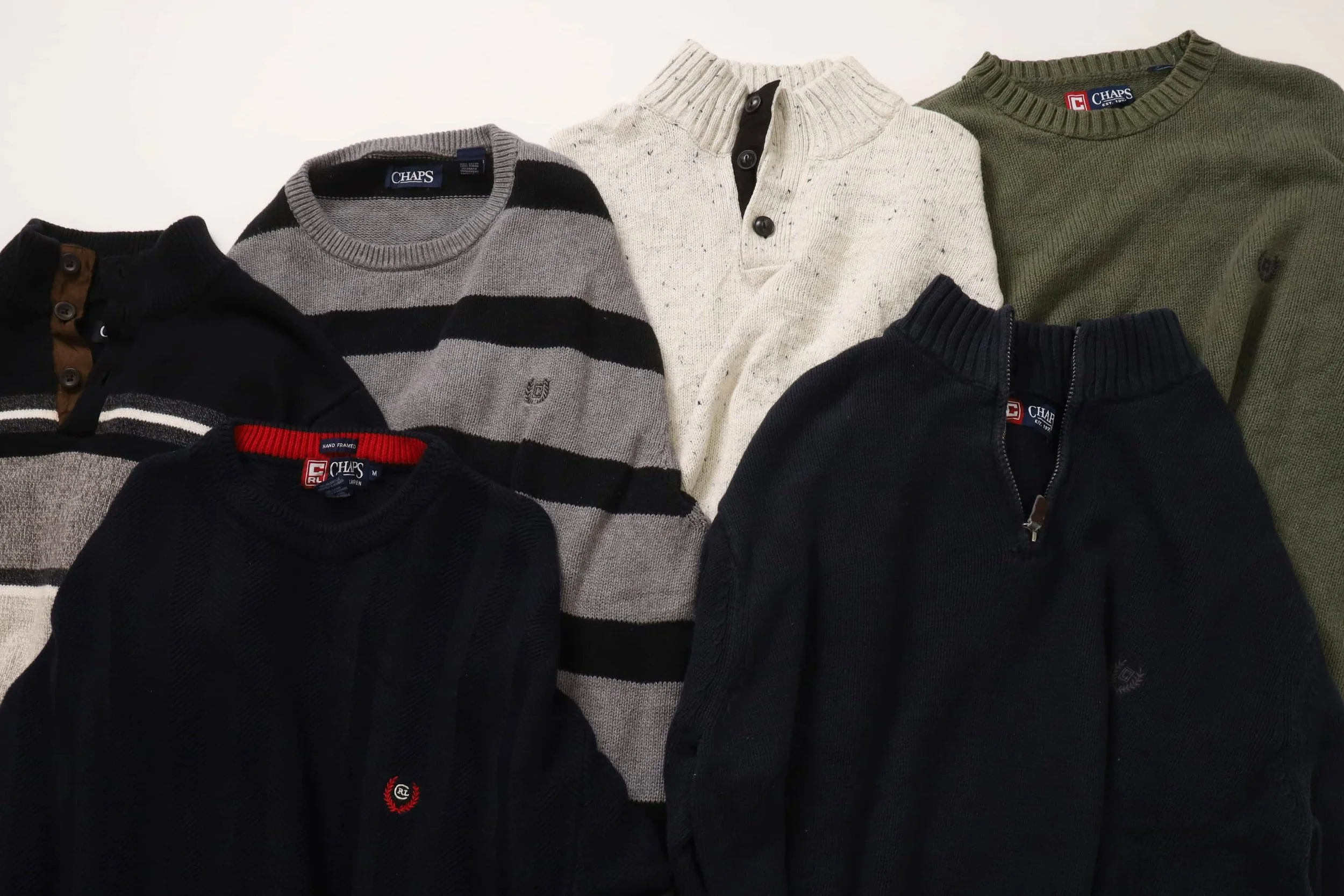 Flat lay of assorted vintage Chaps sweaters in navy, grey, cream, and olive tones, photographed for the Foundry Archives AW25 drop.