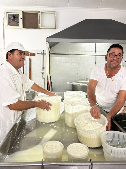 Två män i ett kök, som tillverkar Ricotta ost i stora plastbehållare i Sicilien. 