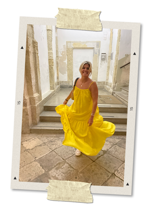 Woman in a bright yellow dress standing on stone steps in an old building with peeling white walls.