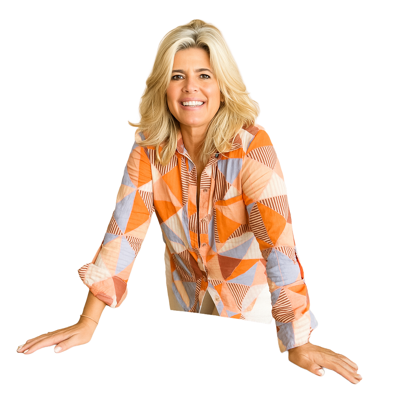 A smiling woman with blonde hair wearing a colorful geometric patterned shirt leaning forward on a table with both hands.