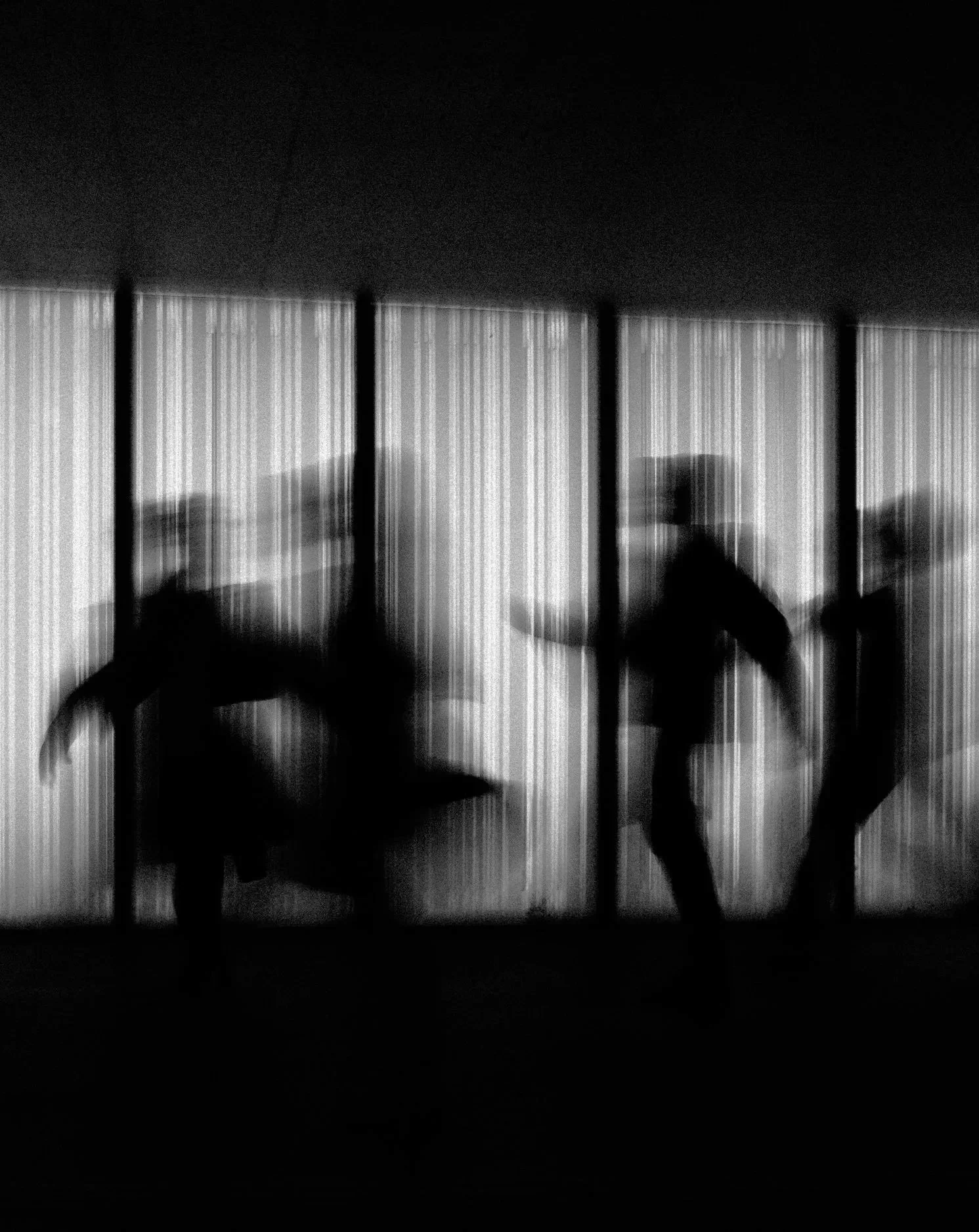 Silhouettes of three people in motion, behind a striped, semi-transparent partition.