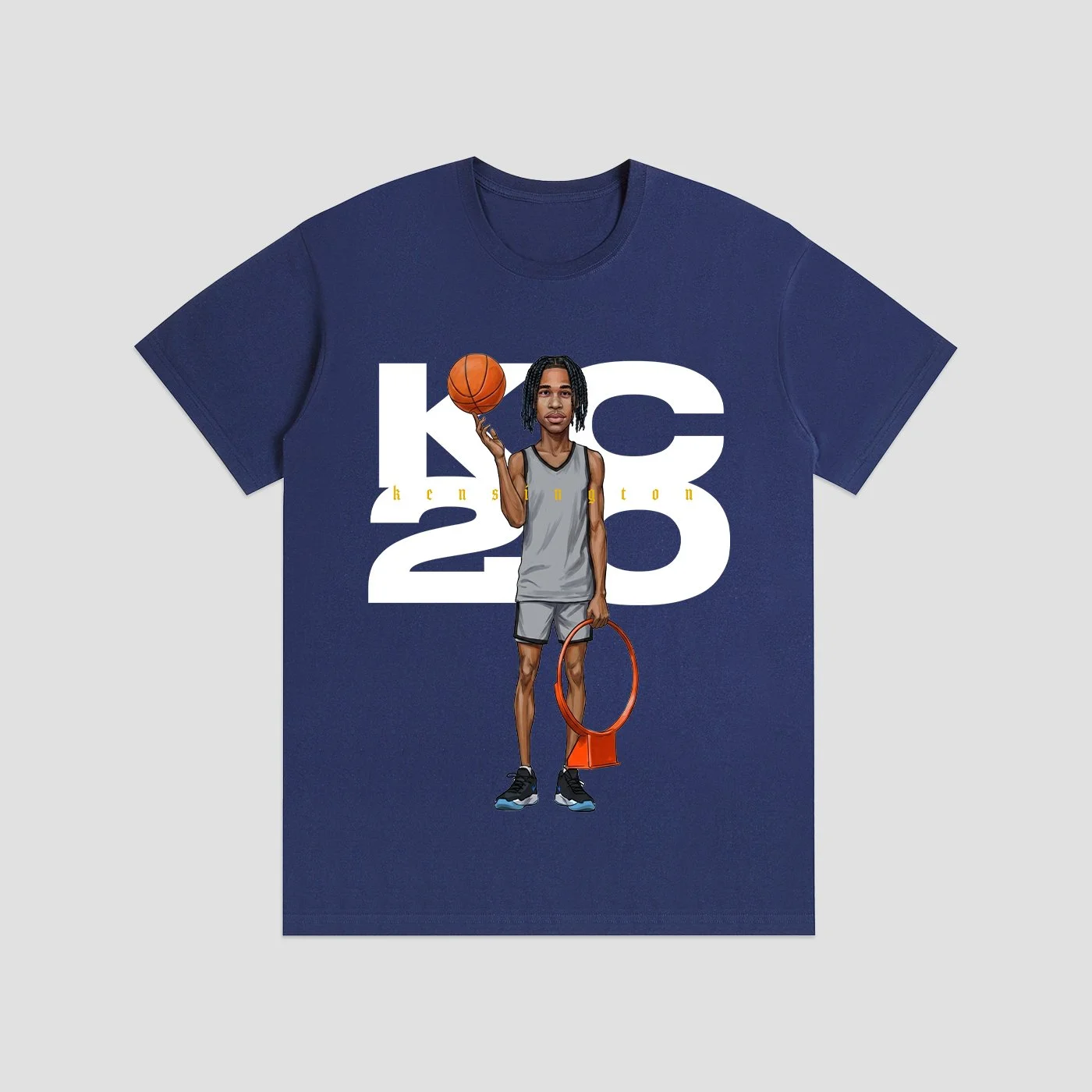 Blue T-shirt featuring an illustration of a basketball player holding a basketball and a hoop, with the text 'KC 20' in large white letters and the name 'Kensington' in small yellow letters.