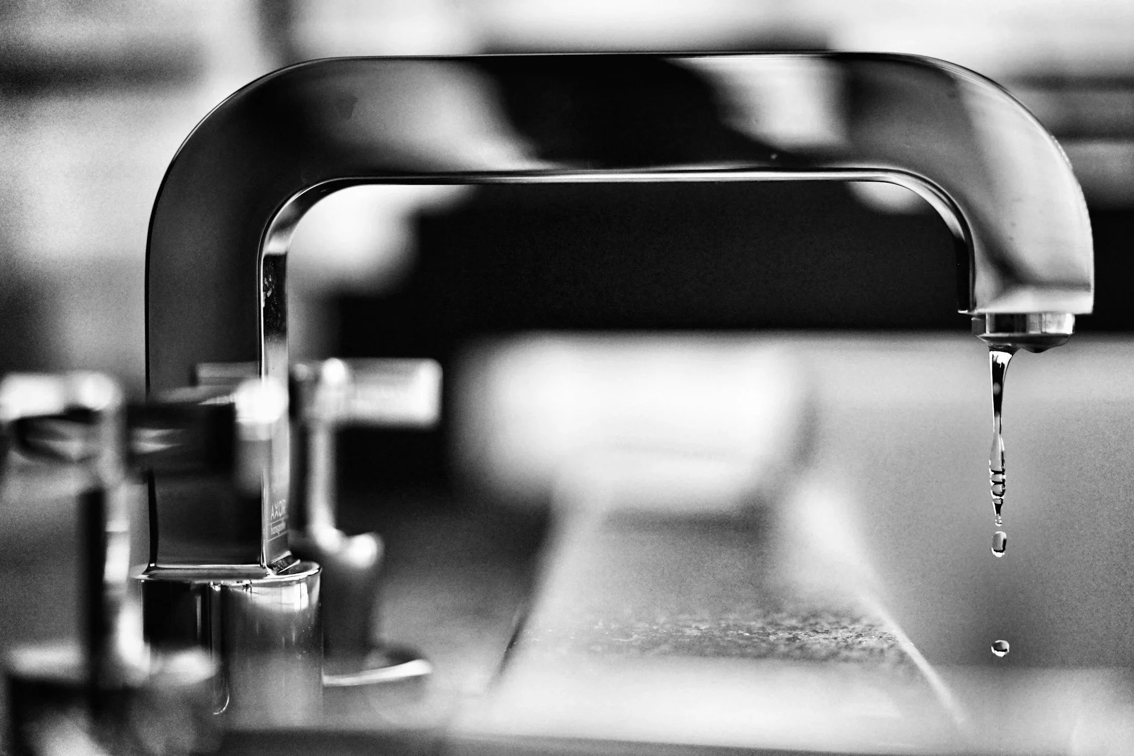 Close-up of a kitchen sink faucet with a small stream of water droplets falling from it in black and white.