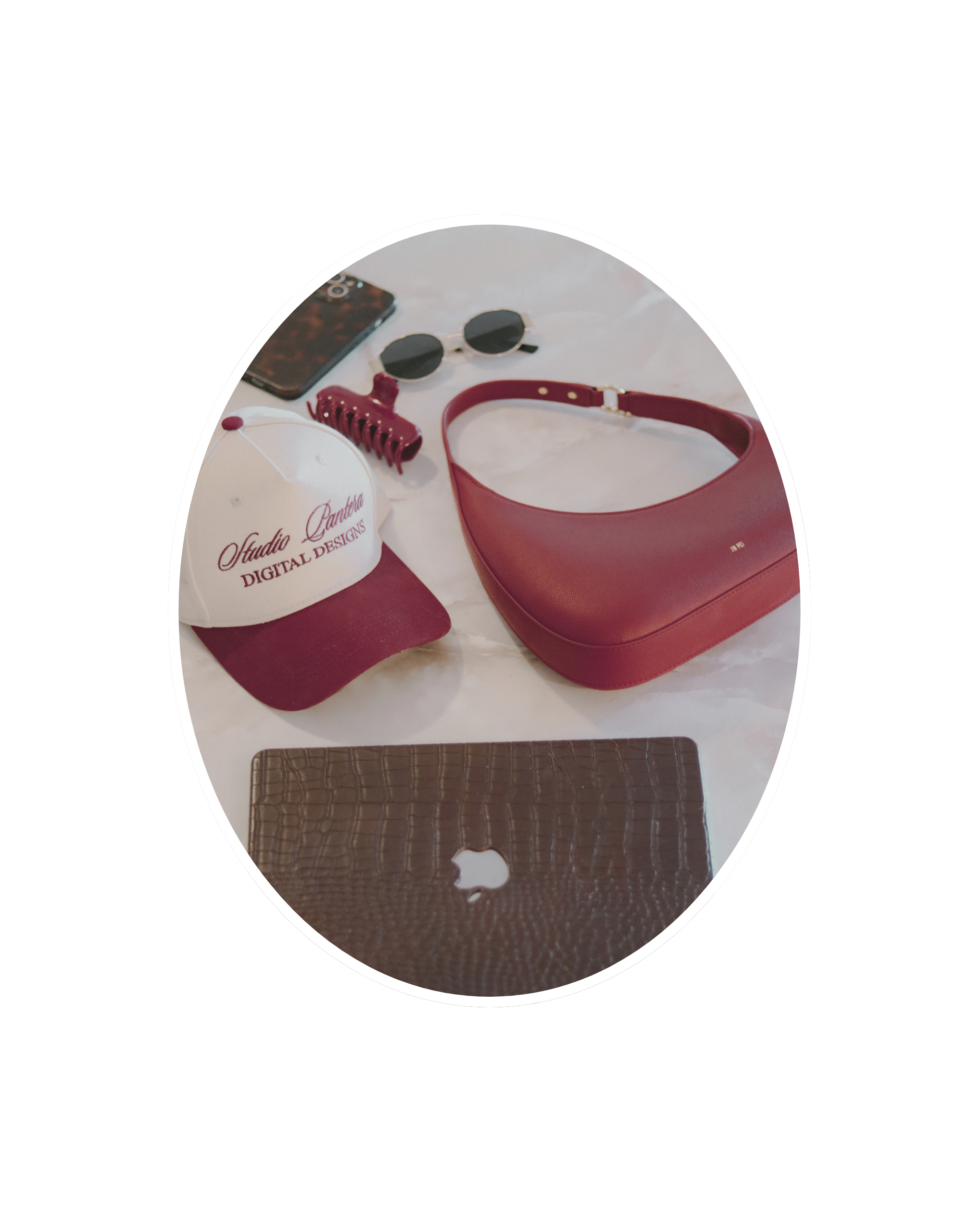 A collection of personal items on a white surface, including a white baseball cap with red text, a pair of black sunglasses, a red hair clip, a red handbag, a branded phone case, and a crocodile-textured brown laptop.