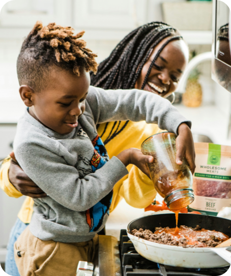 Mom and young boy cooking ground meat in a skillet together in the kitchen.