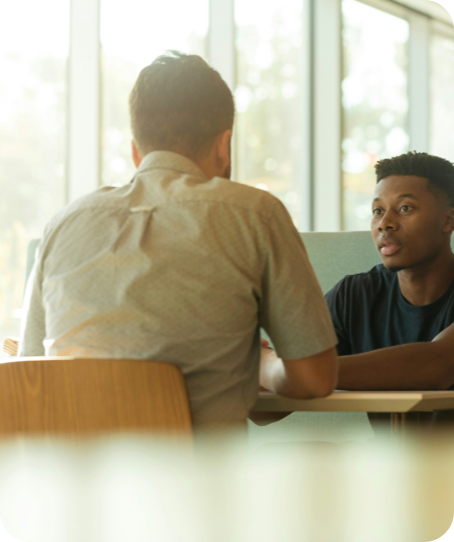 Two men having a conversation at a table near a window.