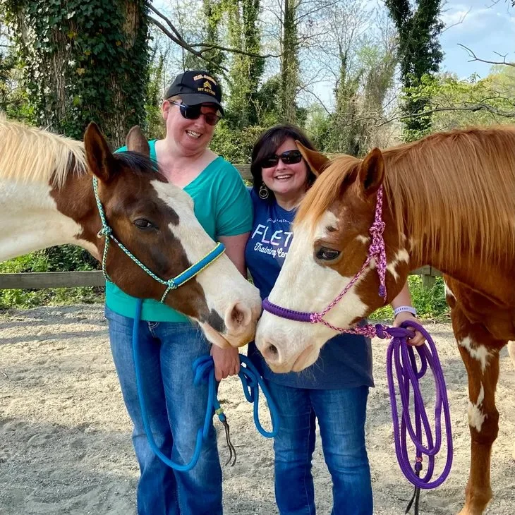 Two women smiling alongside two horses