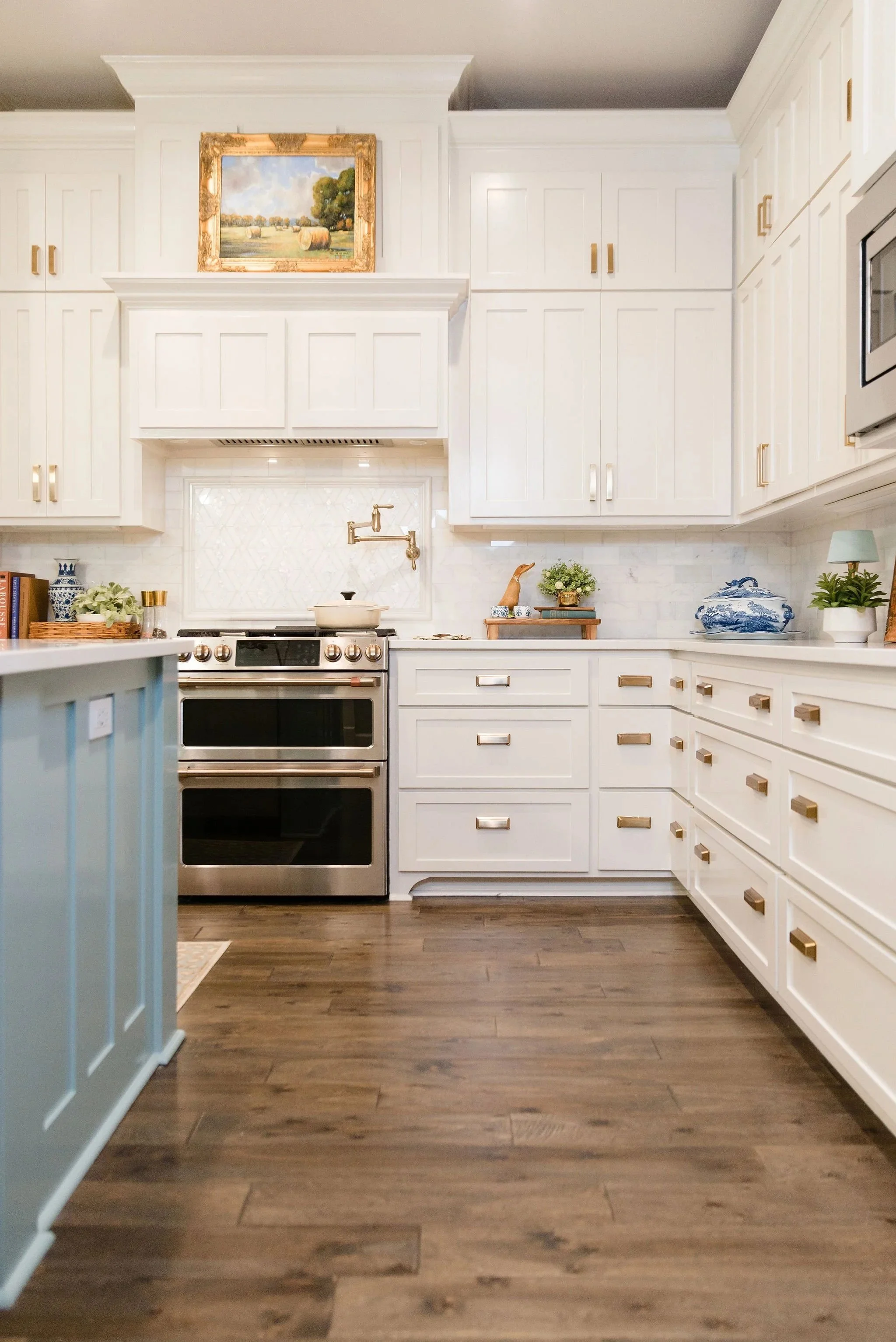 Bright white kitchen with gold hardware, dark wooden floor, and decorative artwork above the cabinets.
