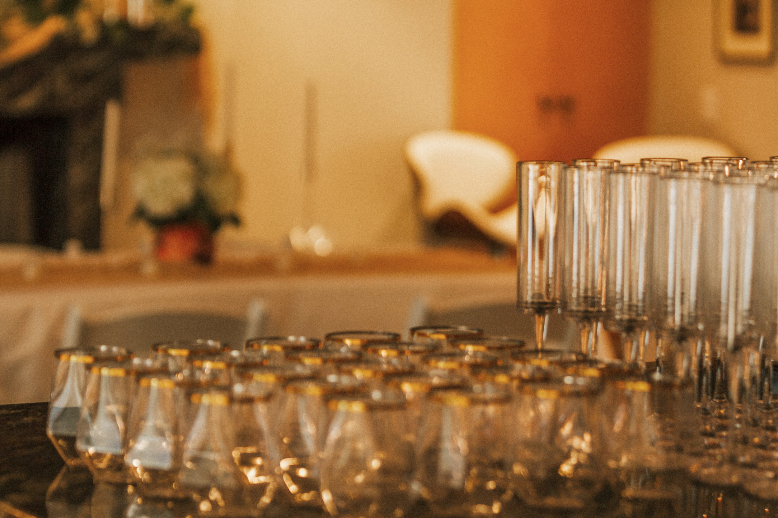 Multiple empty glasses and shot glasses on a dark bar or table with a blurred background of a cozy room.