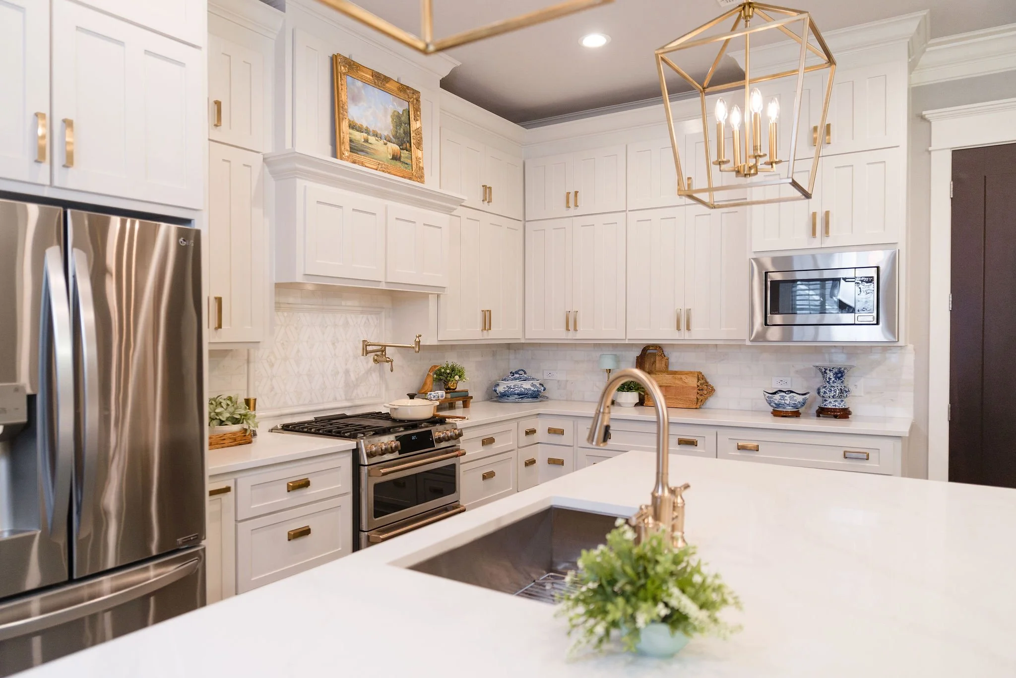 Kitchen with white cabinets and marble countertops, featuring a stainless steel refrigerator, microwave, stove, and a modern brass chandelier.